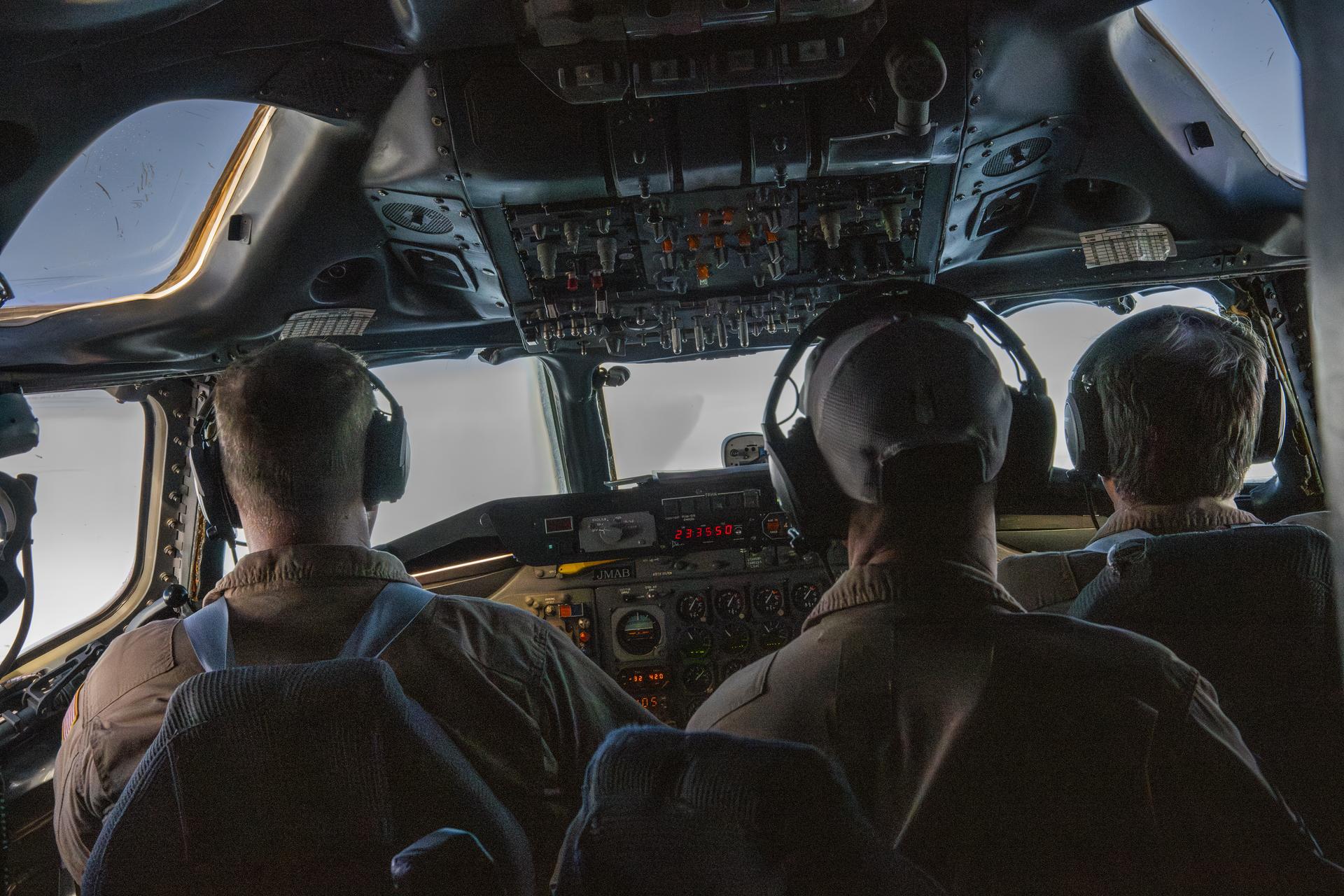 Uma visão por trás de três homens dentro da cabine de comando do DC-8 e pela janela frontal enquanto eles executam o plano durante a campanha de testes de rastros.