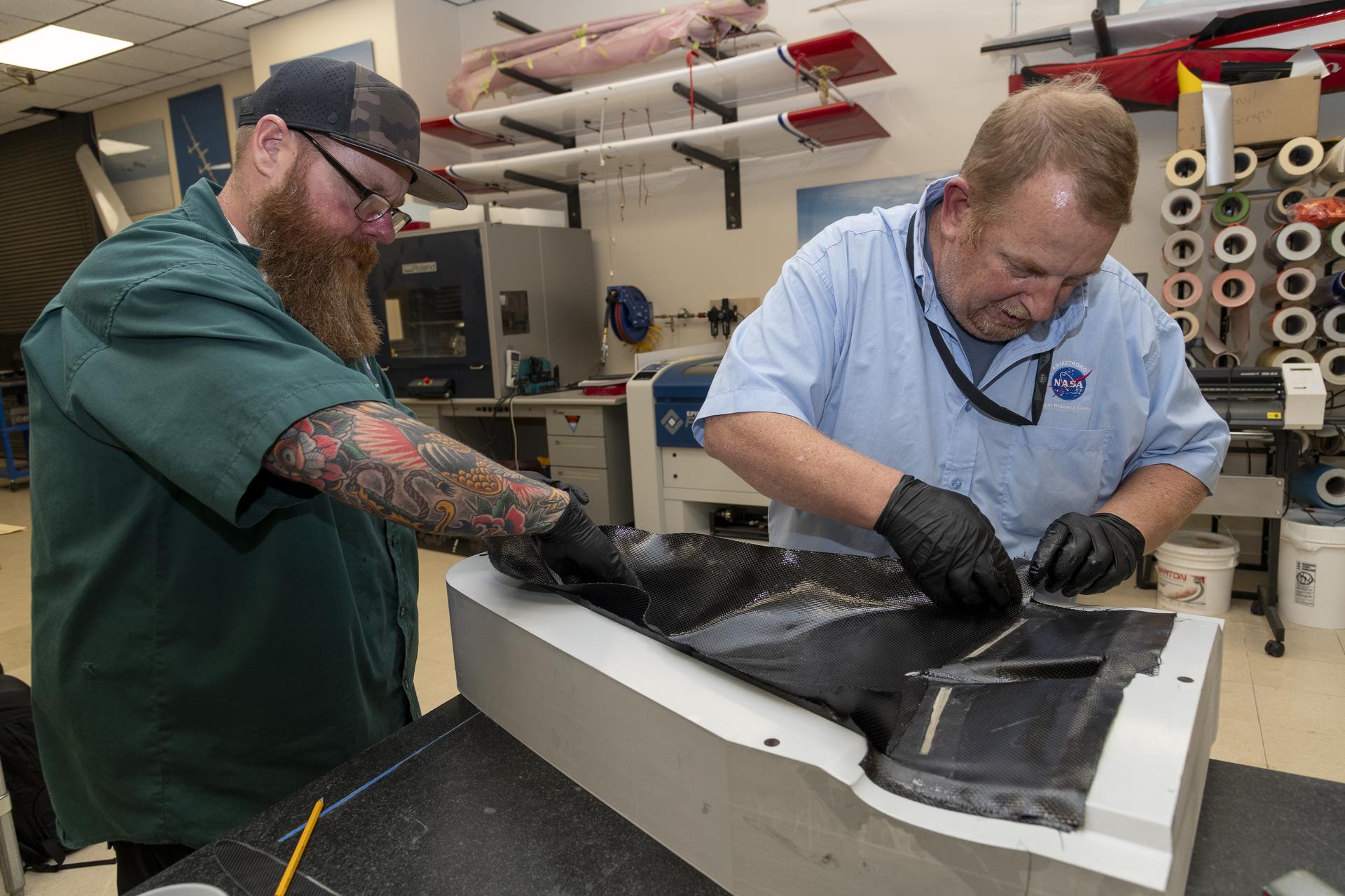 Two men layer composite material on an aircraft model mold.