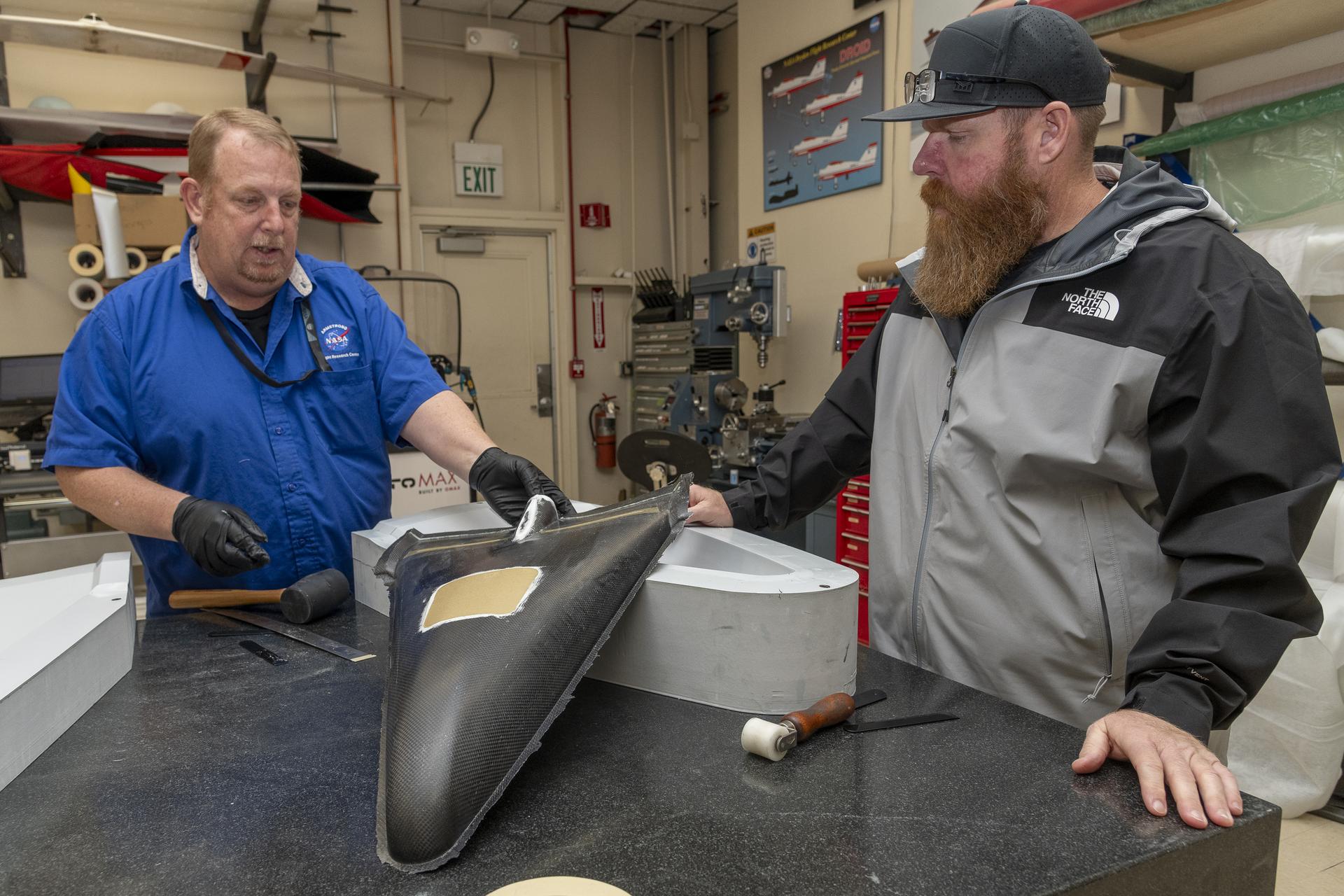 Two men take a major section of an aircraft model out of a mold.