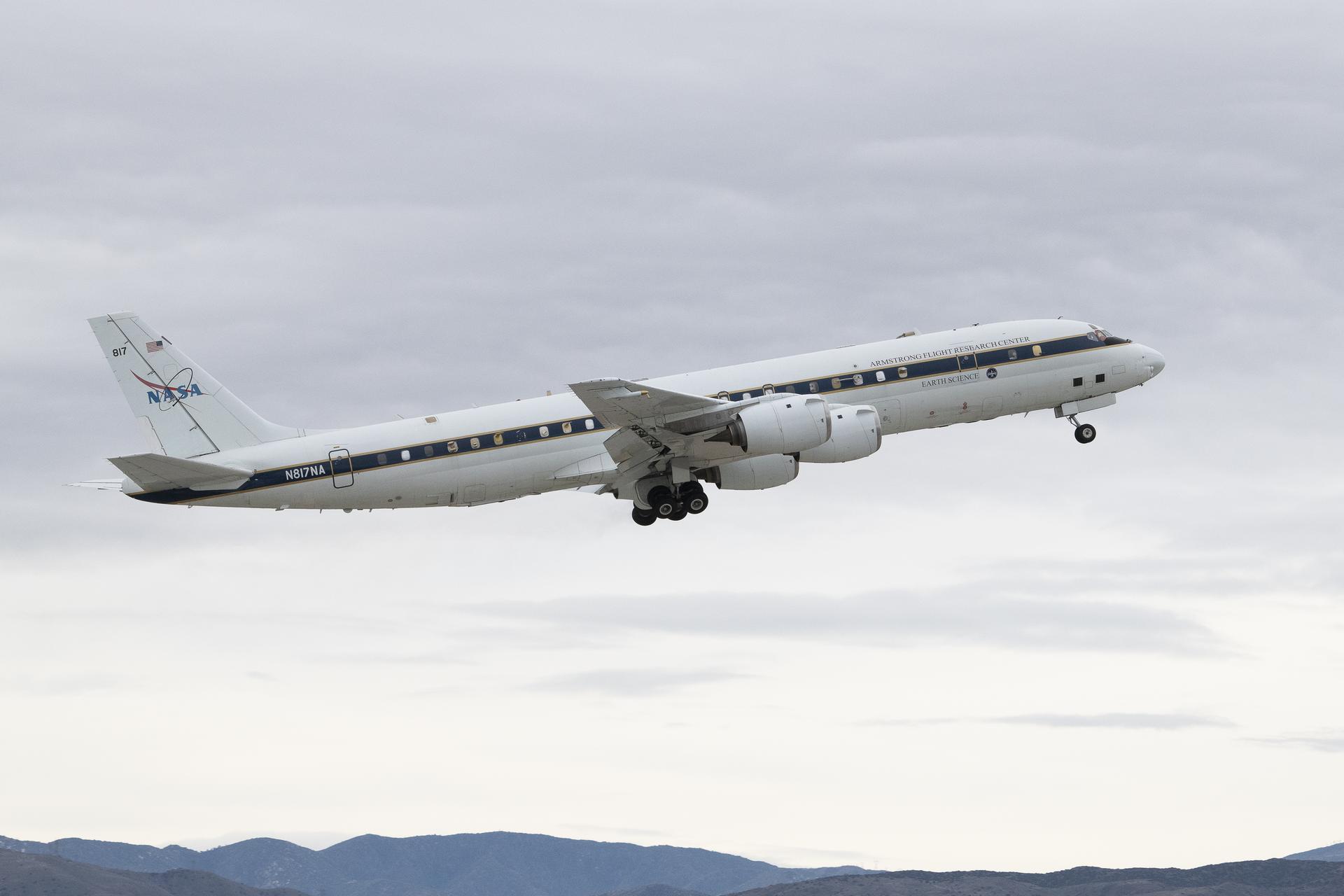 The DC-8 aircraft takes off from Palmdale, California, ascending against a cloudy gray sky