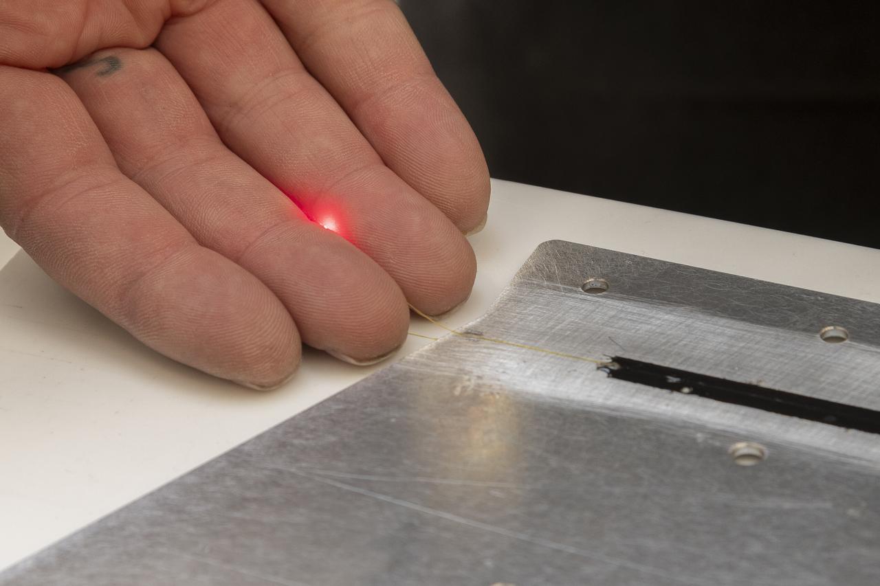 A red light confirms that the fiber of the Fiber Optic Sensing System installed on the Mock Truss-Braced Wing 10-foot model works as intended at NASA’s Armstrong Flight Research Center in Edwards, California. The fiber, which is about the thickness of a human hair, is part of a system that can provide strain information researchers can use to determine the model’s durability.