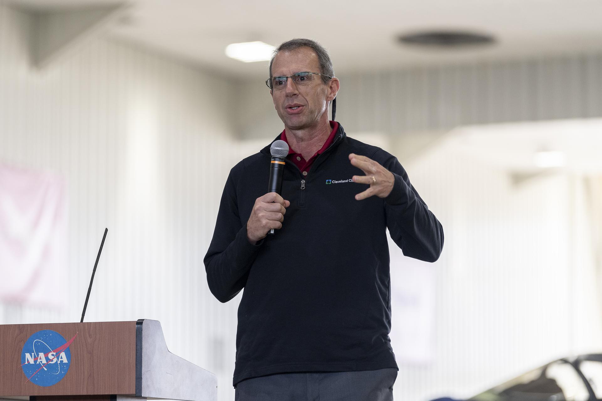 A man talks at a podium in an aircraft hangar.