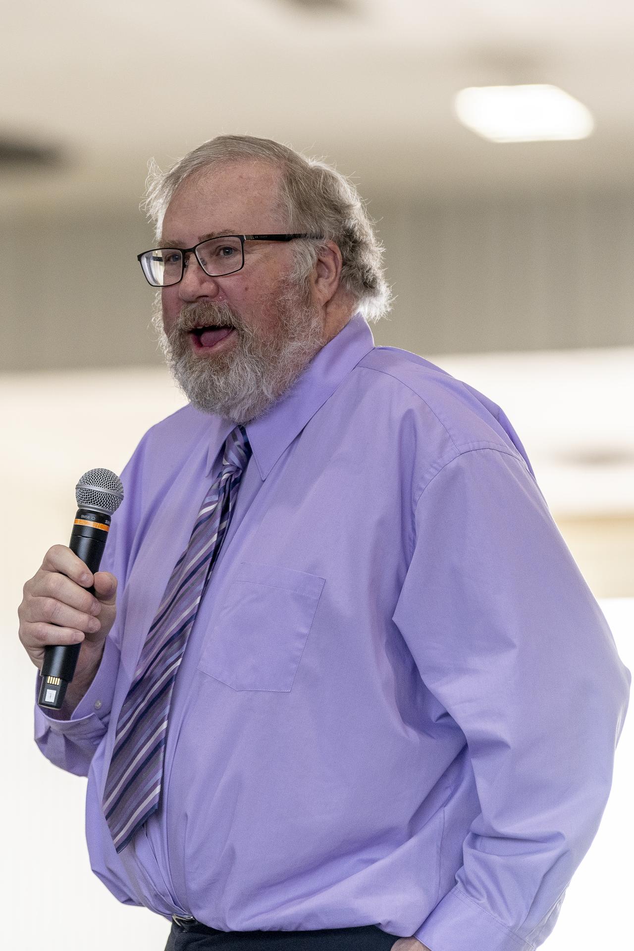 A man talks at a podium in an aircraft hangar.