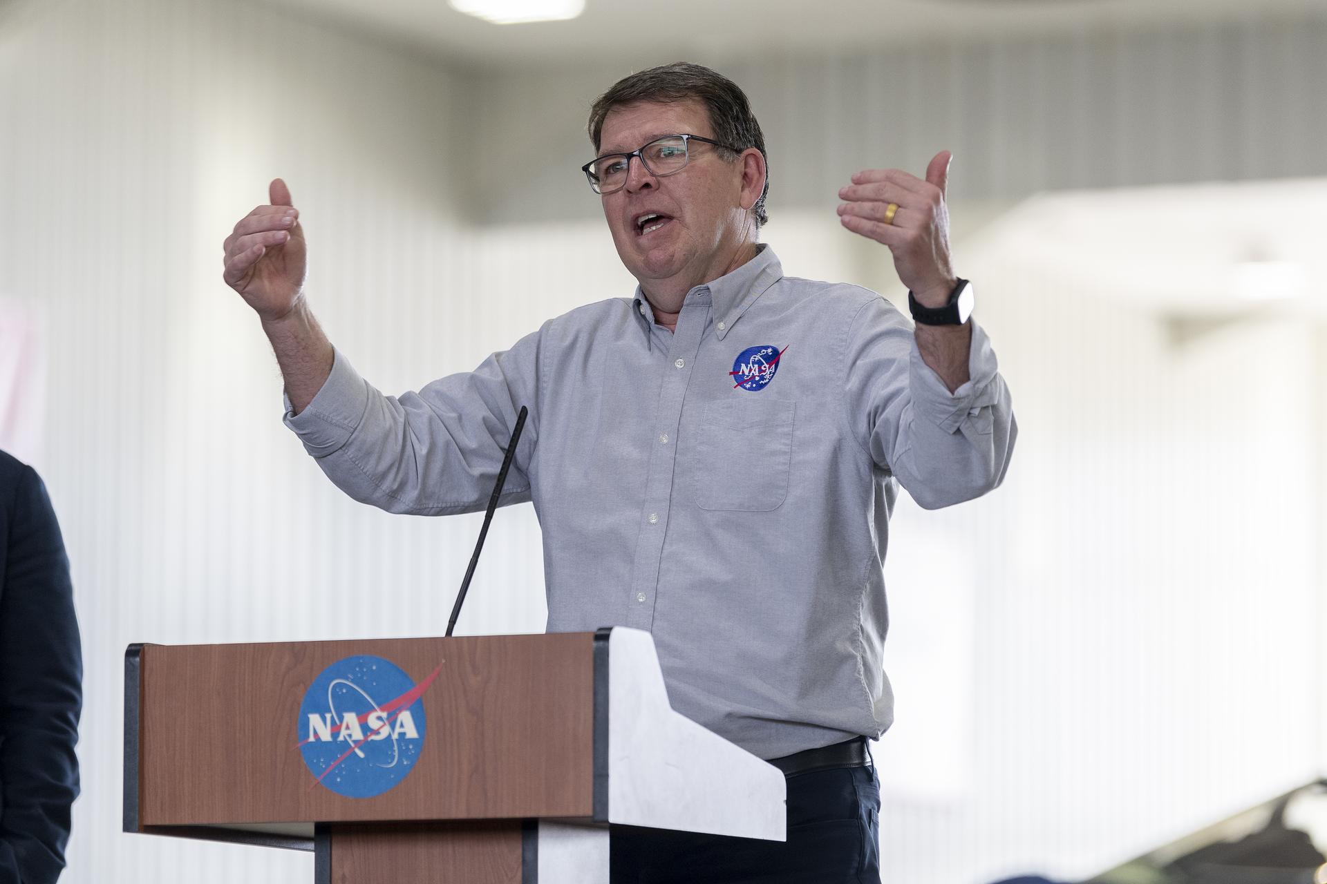 A man talks at a podium in an aircraft hangar.