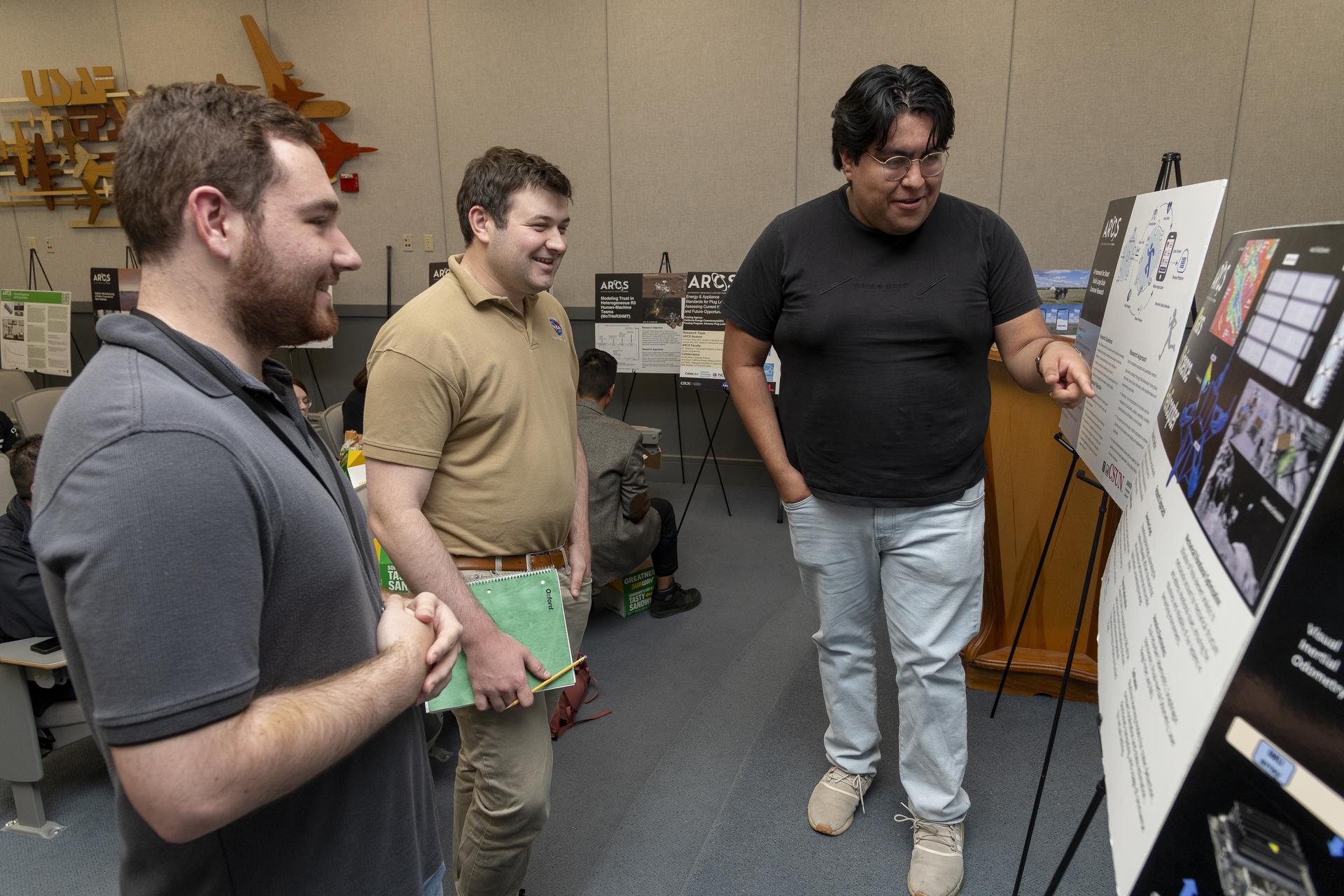 Two men ask a third man about his technology poster.