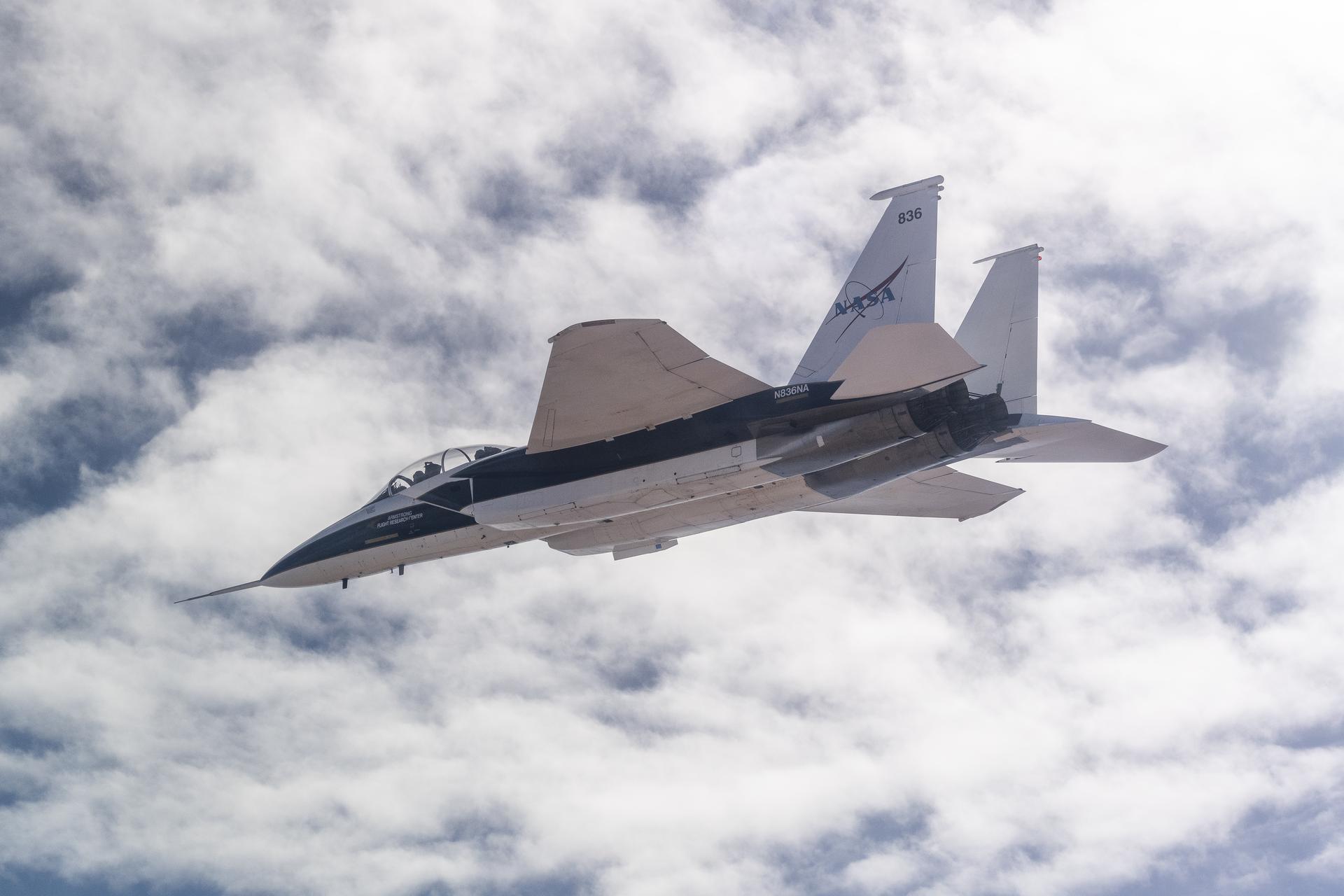 An F-15B aircraft, painted white and blue, is shown in flight with clouds above. The Shock Sensing Probe mounted to its nose during an Aug. 6, 2024, calibration flight over Edwards, California.