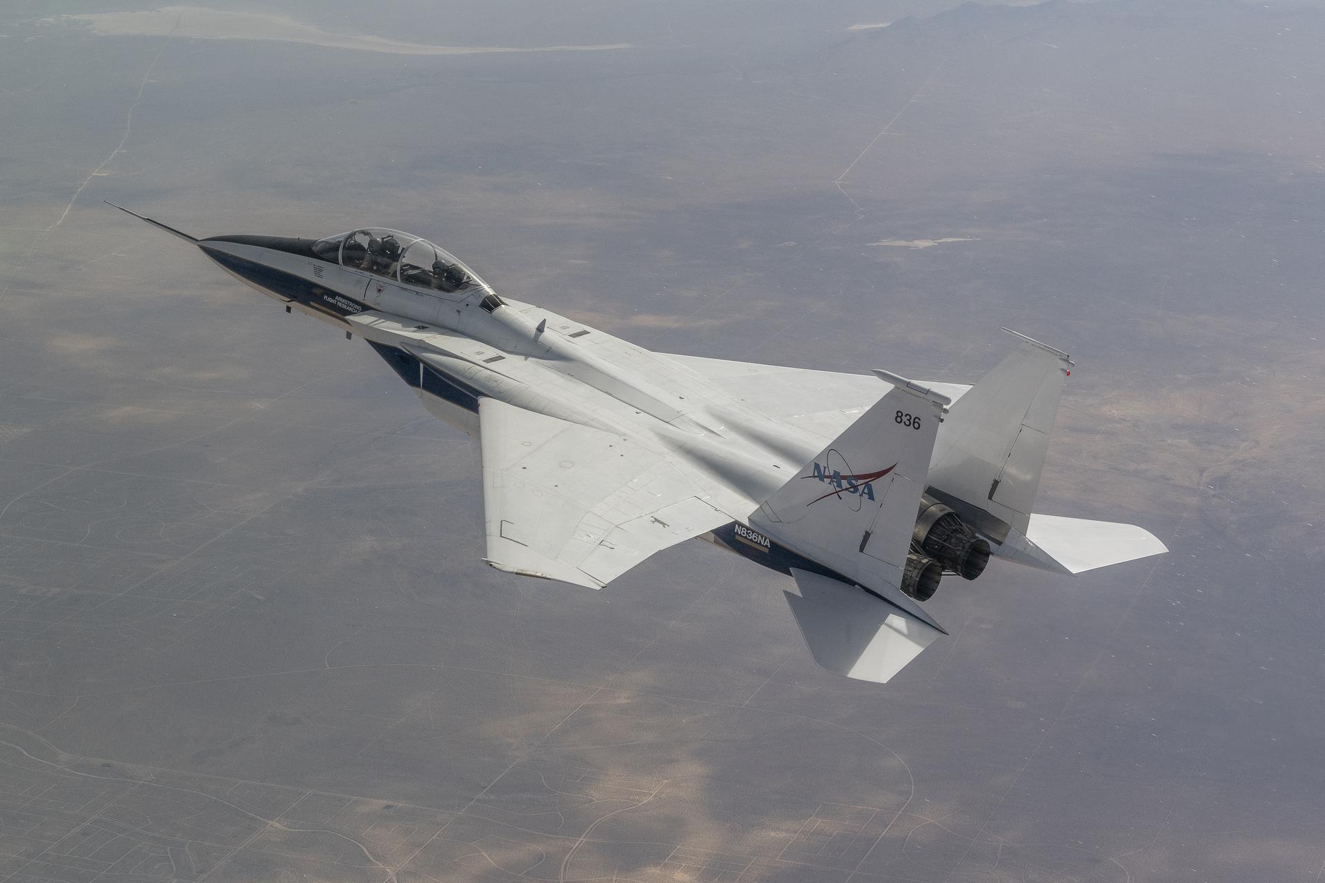 An F-15B aircraft, painted white and blue, is shown in flight with clouds above. The Shock Sensing Probe mounted to its nose during an Aug. 6, 2024, calibration flight over Edwards, California.