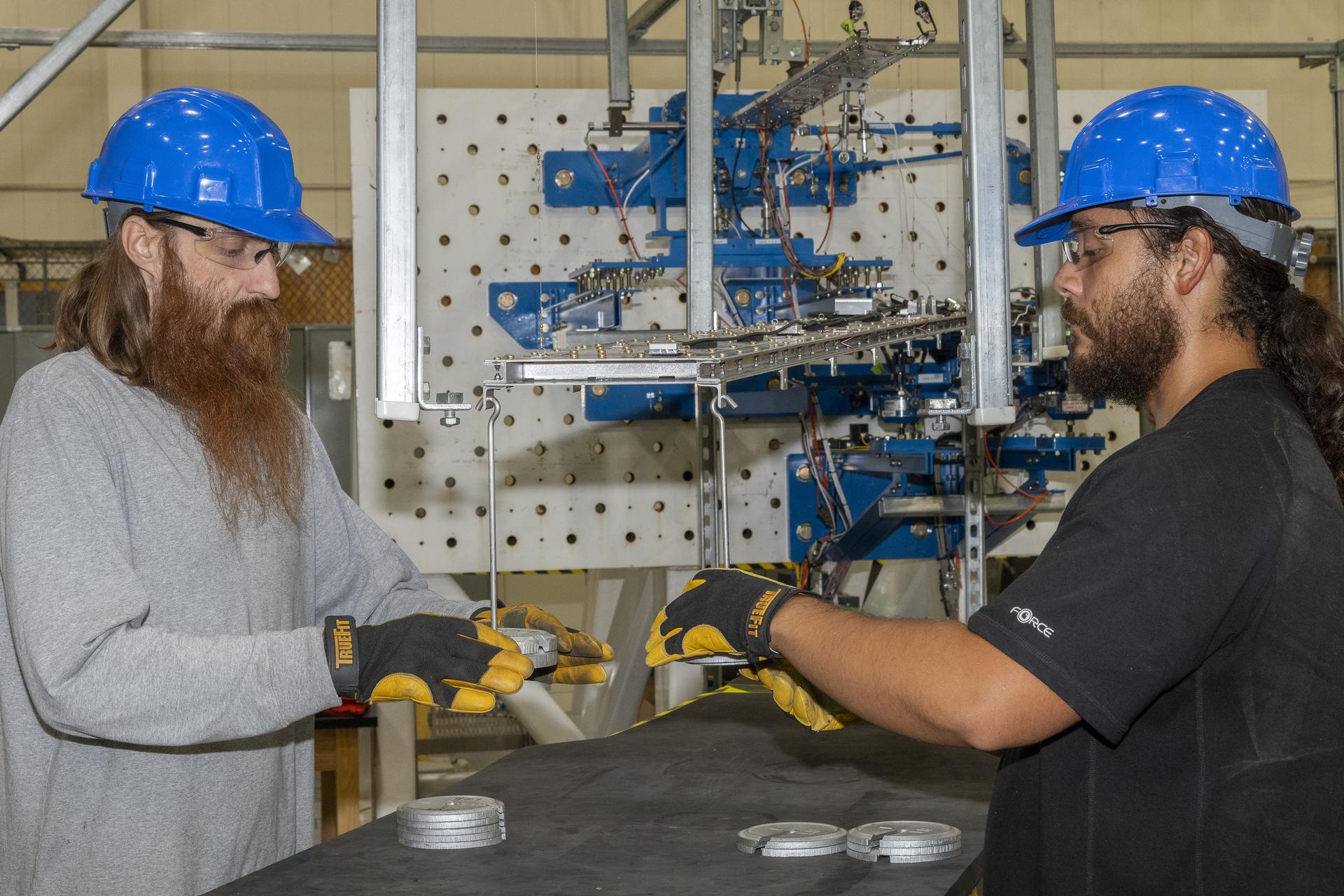 Two men add weight to a wing test article at the same time.