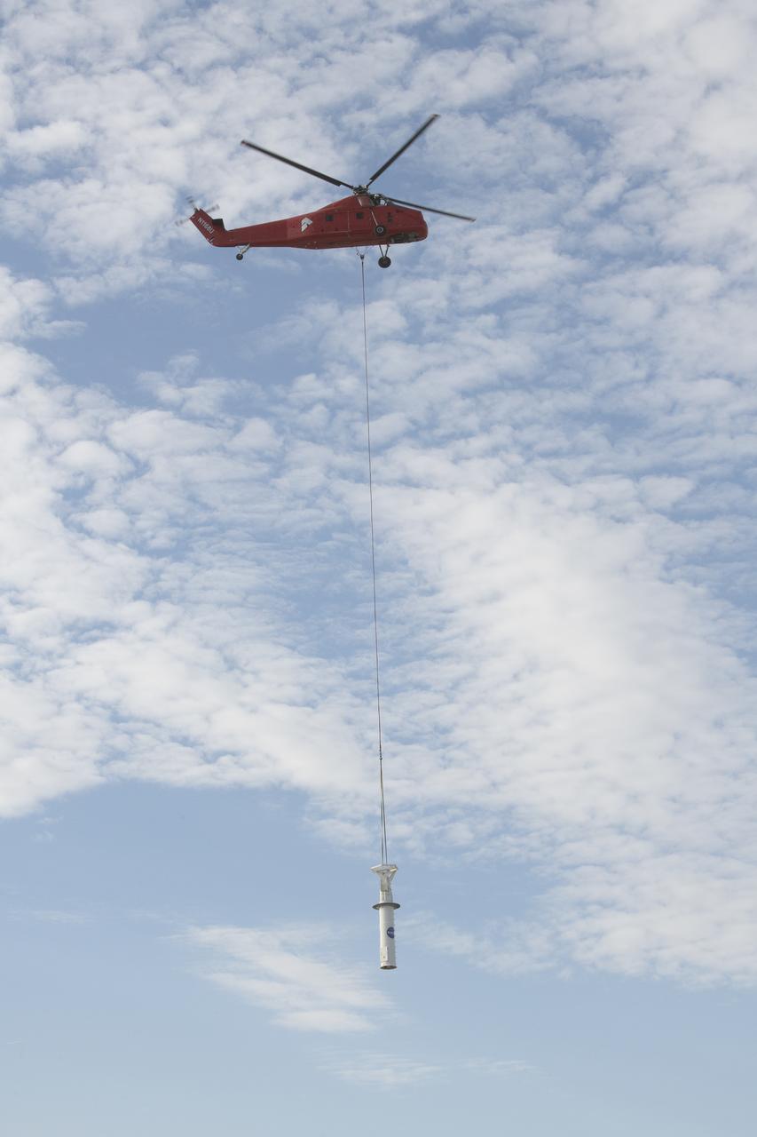 A helicopter carries a rooftop pedestal it removed from Building 4800 at NASA’s Armstrong Flight Research Center in Edwards, California, on Oct. 4, 2024. The pedestal was used since the 1950s to 2015 to house different telemetry dishes to collect data from research aircraft.