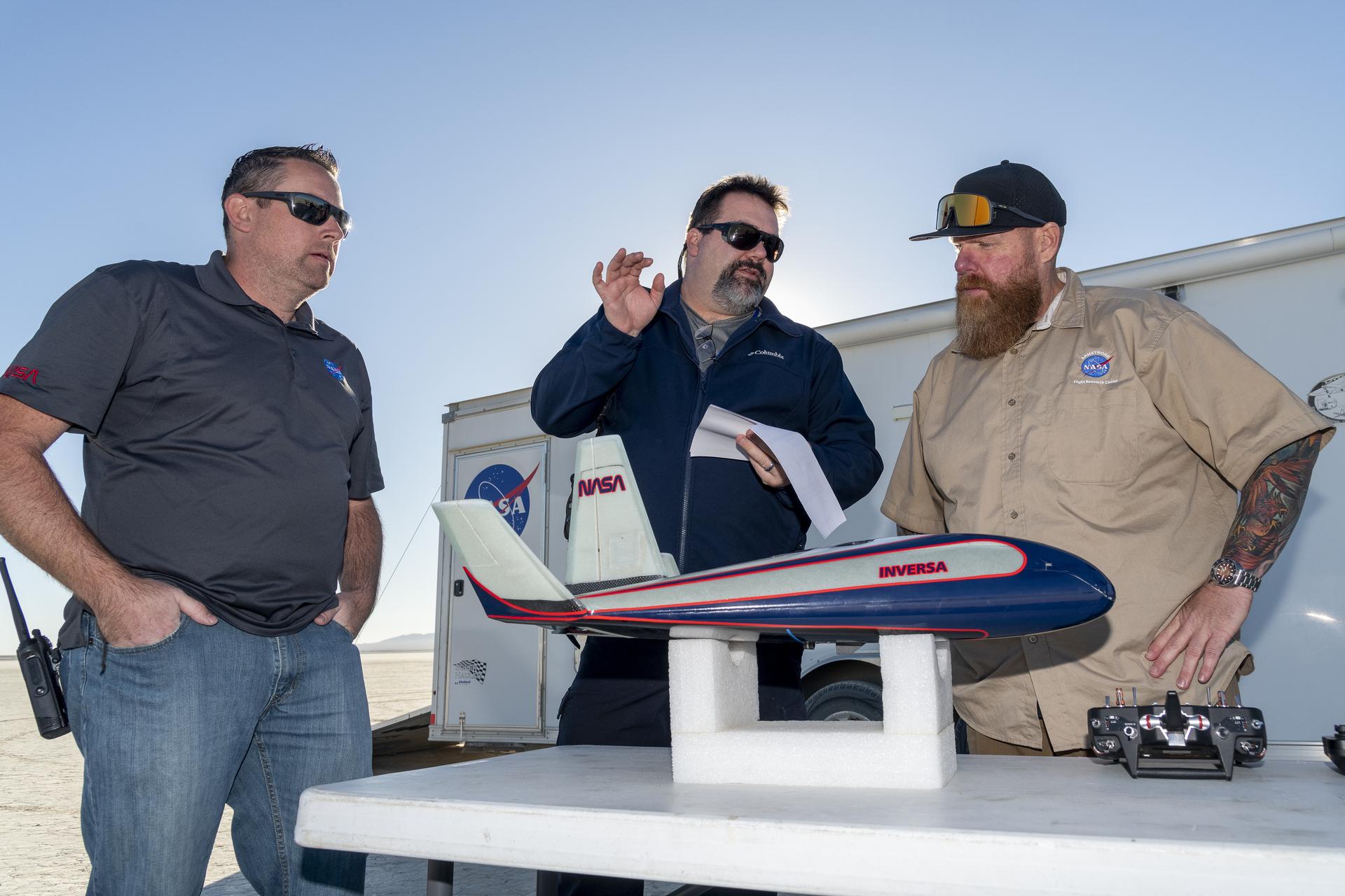 Three men talk with a model probe on the table in front of them.