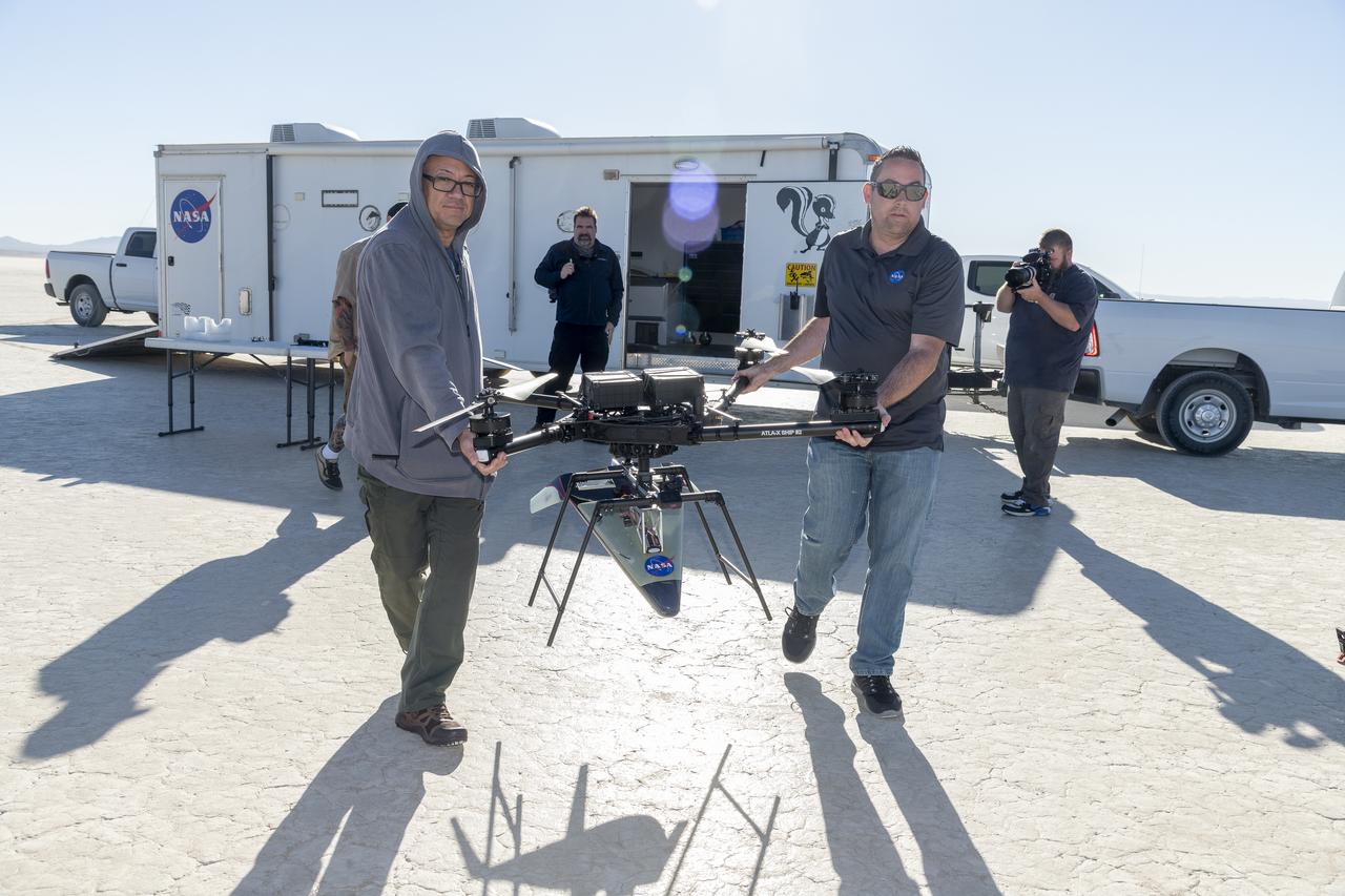Derek Abramson, left, chief engineer for the Dale Reed Subscale Flight Research Laboratory, and Justin Link, small unmanned aircraft system pilot, carry the atmospheric probe model and a quad rotor remotely piloted aircraft to position it for flight on Oct. 24, 2024. John Bodylski, probe principal investigator, right, and videographer Jacob Shaw watch the preparations. Once at altitude, the quad rotor aircraft released the probe above Rogers Dry Lake, a flight area adjacent to NASA’s Armstrong Flight Research Center in Edwards, California. The probe was designed and built at the center.