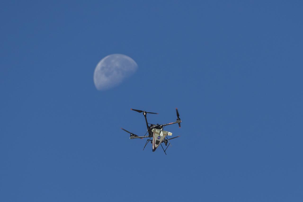 An atmospheric probe model attached upside down to a quad rotor remotely piloted aircraft ascends with the Moon visible on Oct. 22, 2024. The quad rotor aircraft released the probe above Rogers Dry Lake, a flight area adjacent NASA’s Armstrong Flight Research Center in Edwards, California. The probe was designed and built at the center.