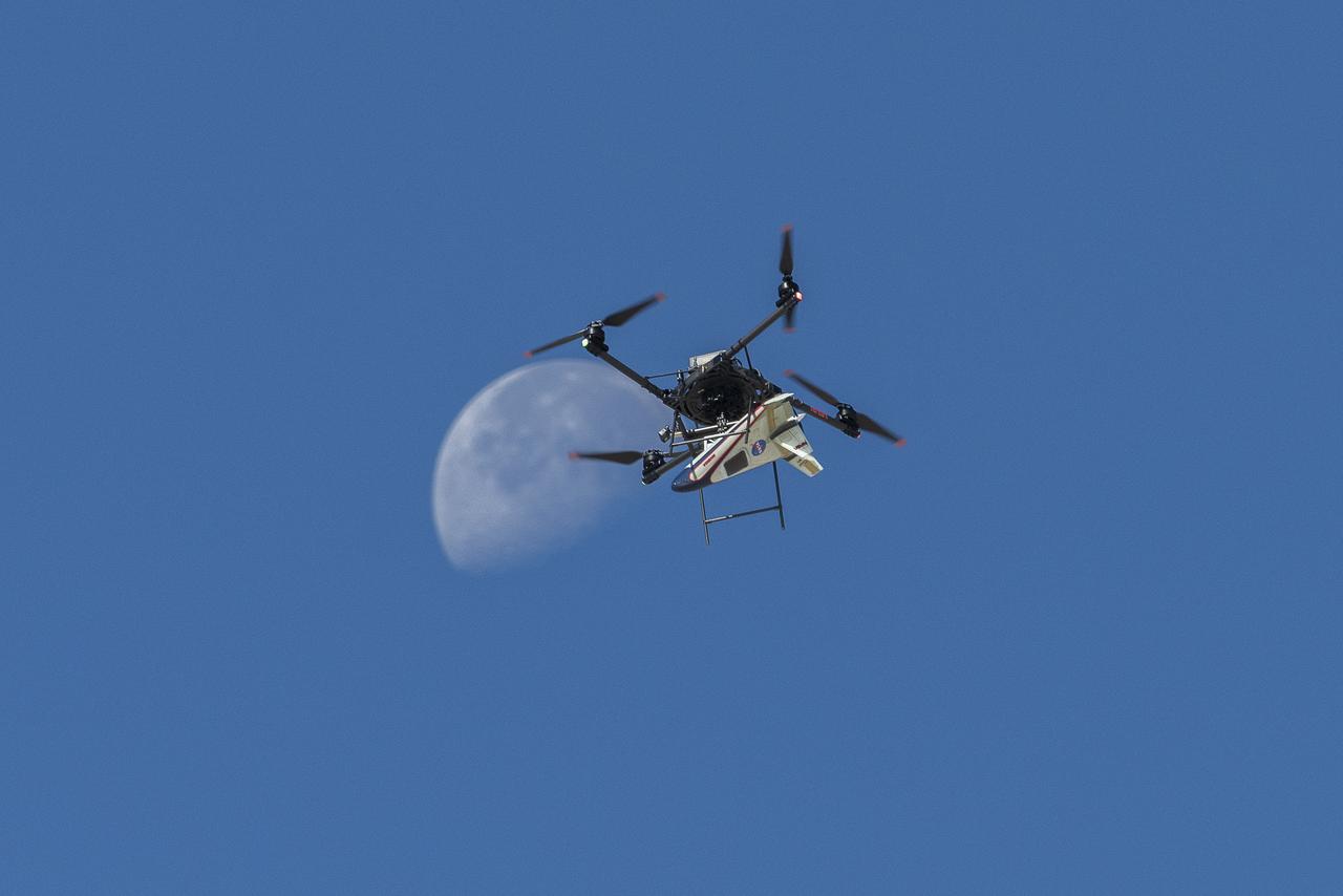 An atmospheric probe model attached upside down to a quad rotor remotely piloted aircraft ascends with the Moon visible on Oct. 22, 2024. The quad rotor aircraft released the probe above Rogers Dry Lake, a flight area adjacent NASA’s Armstrong Flight Research Center in Edwards, California. The probe was designed and built at the center.