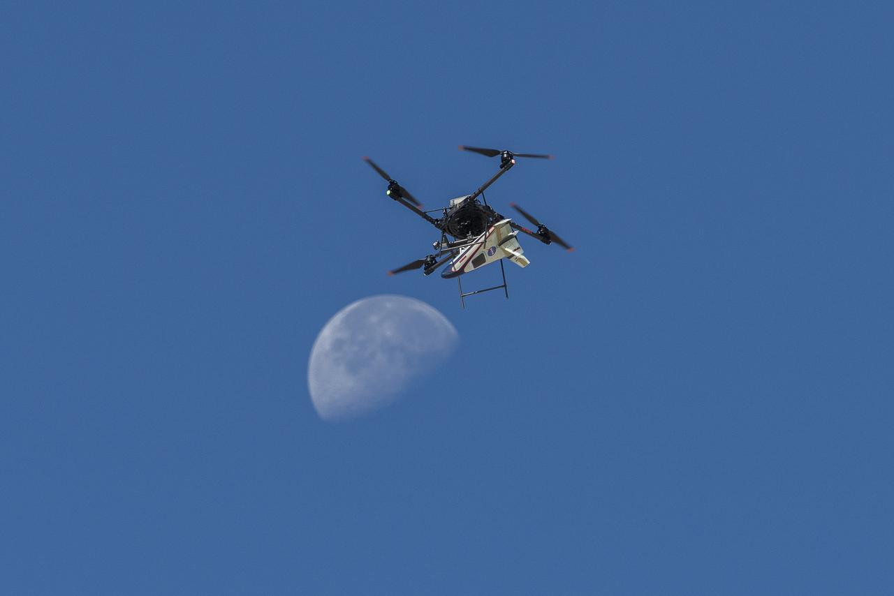 An atmospheric probe model attached upside down to a quad rotor remotely piloted aircraft ascends with the Moon visible on Oct. 22, 2024. The quad rotor aircraft released the probe above Rogers Dry Lake, a flight area adjacent NASA’s Armstrong Flight Research Center in Edwards, California. The probe was designed and built at the center.