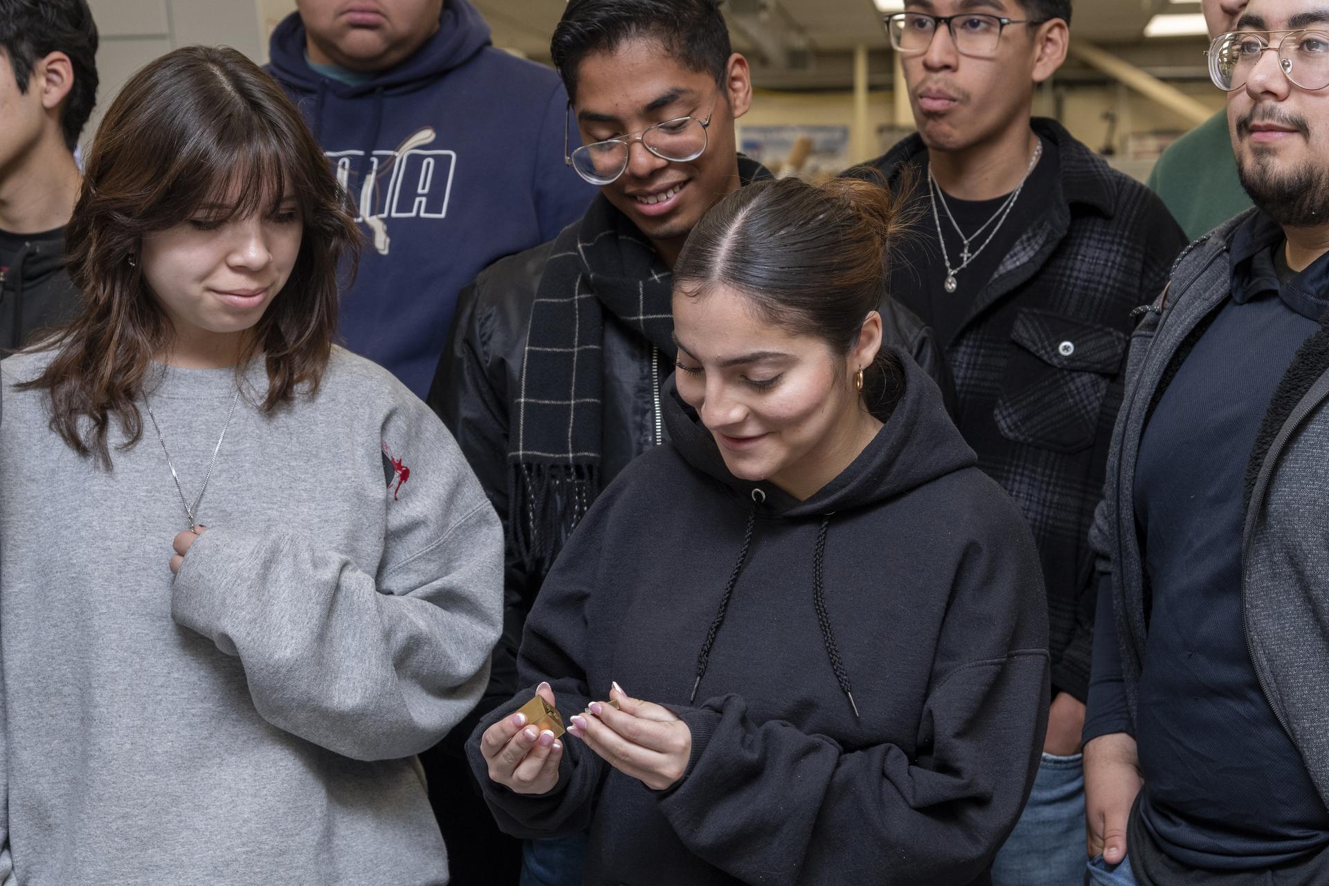 A group of students stand close together to examine a small part.