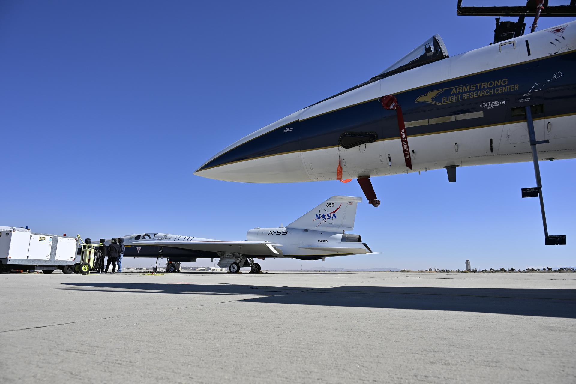 NASA’s X-59 sits partially outside a white hangar at Lockheed Martin’s Skunk Works Facility in Palmdale, California, with cables and sensors extending from its cockpit.