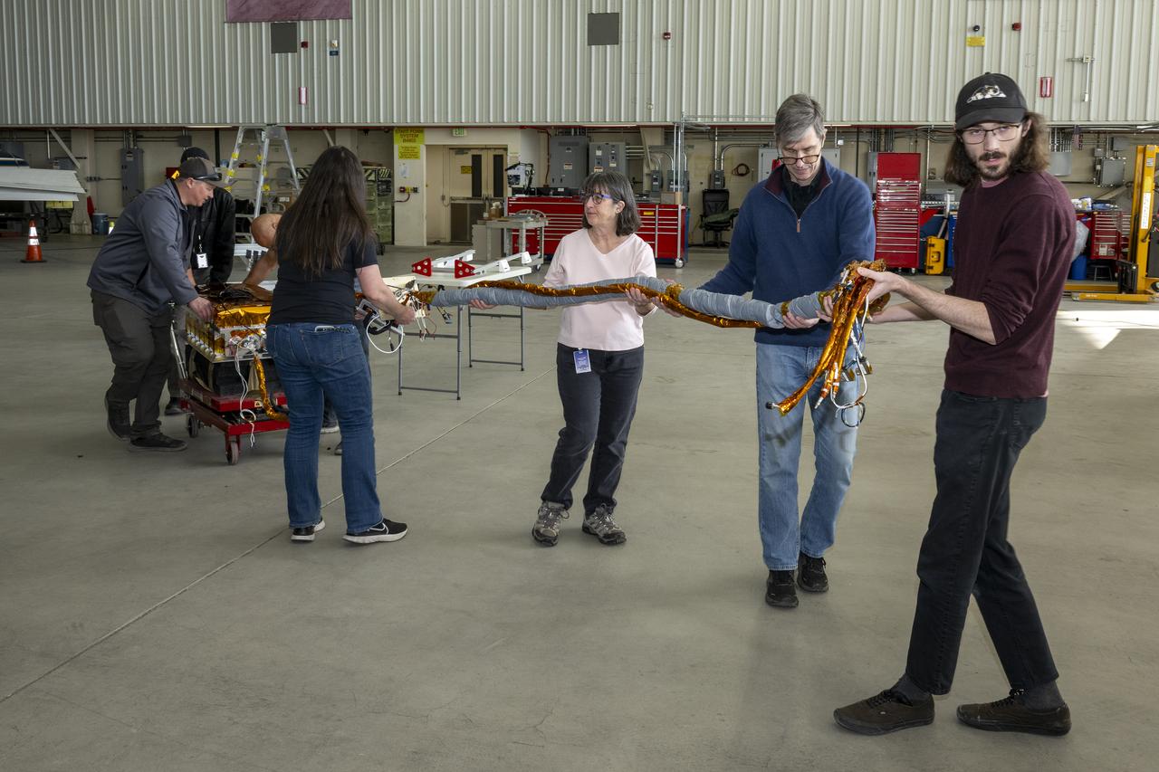 The airborne Lunar Spectral Irradiance (air-LUSI) instrument is moved across the hangar floor by robotic engineer Alexander McCafferty-Leroux ,from right to left, co-investigator Dr. John Woodward, NIST astronomer Dr. Susana Deustua, air-LUSI chief system engineer Dr. Kathleen “Kat” Scanlon, and members of the ER-2 ground crew at NASA’s Armstrong Flight Research Center in Edwards, California, in March 2025.