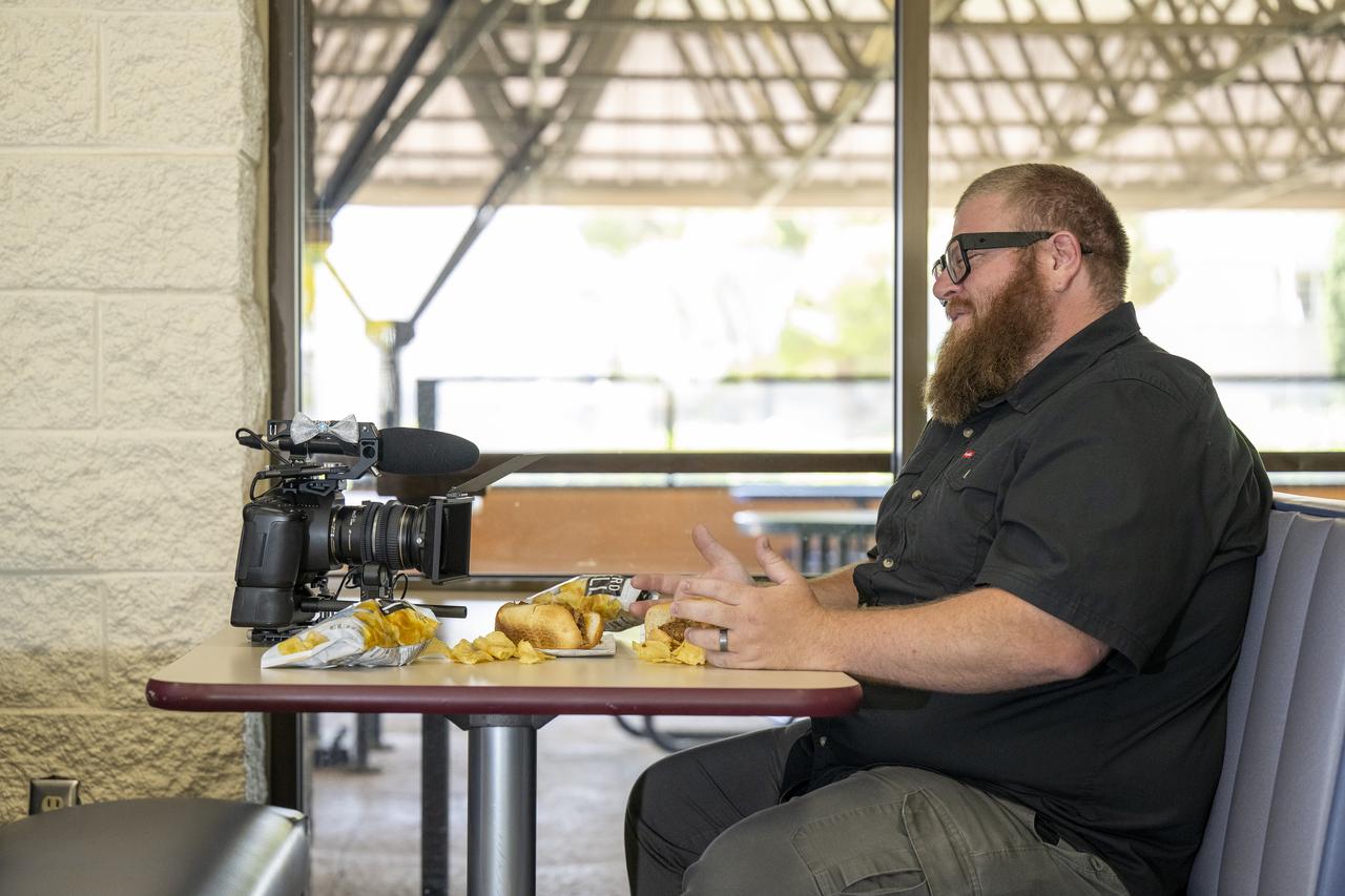 NASA videographer Jacob Shaw shares a moment with his constant companion during a break in the cafeteria at NASA’s Armstrong Flight Research Center in Edwards, California, on May 21, 2025. Shaw recently earned first place in NASA’s 2024 Videographer of the Year Awards – documentation category – for his film, “Reflections,” which chronicles the 2024 Airborne Science mission PACE-PAX – short for Plankton, Aerosol, Cloud, ocean Ecosystem Postlaunch Airborne eXperiment.