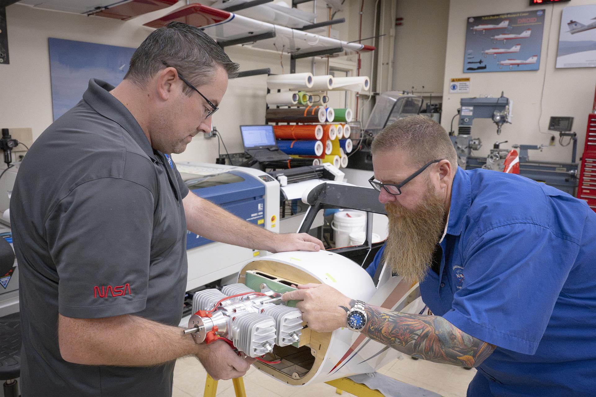 Two men attach an engine onto a subscale aircraft.
