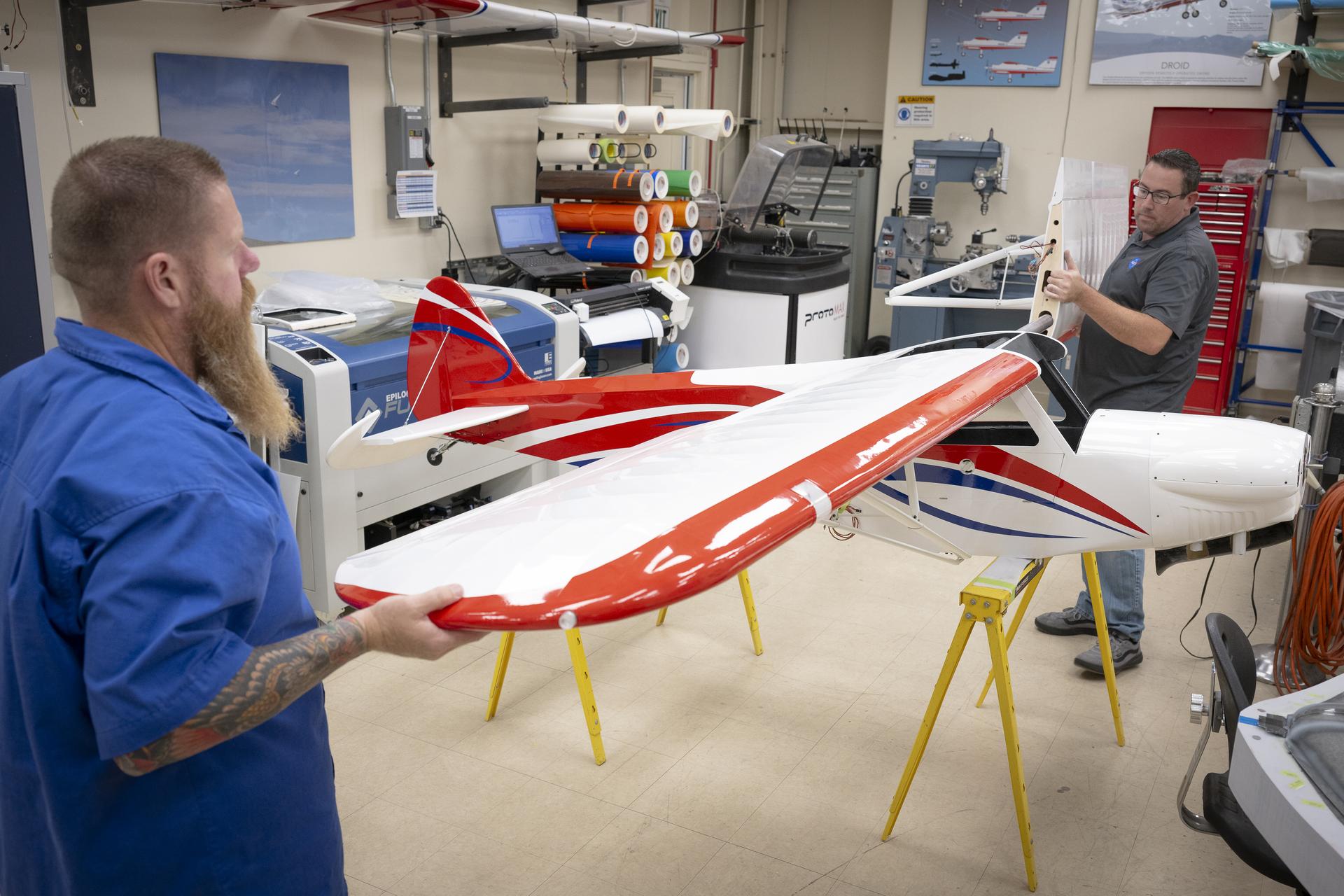 Two men attach an engine onto a subscale aircraft.