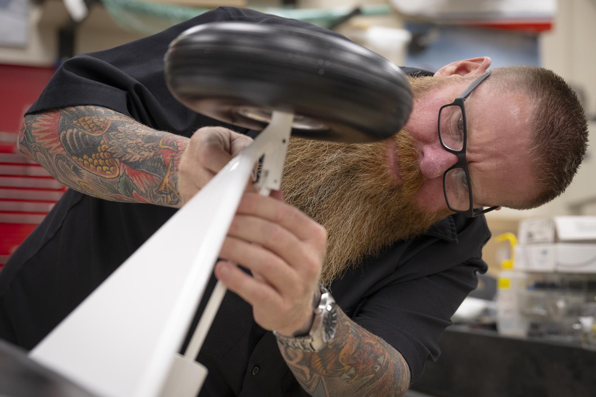 A man attaches a wheel and a section of landing gear to a subscale aircraft during assembly.