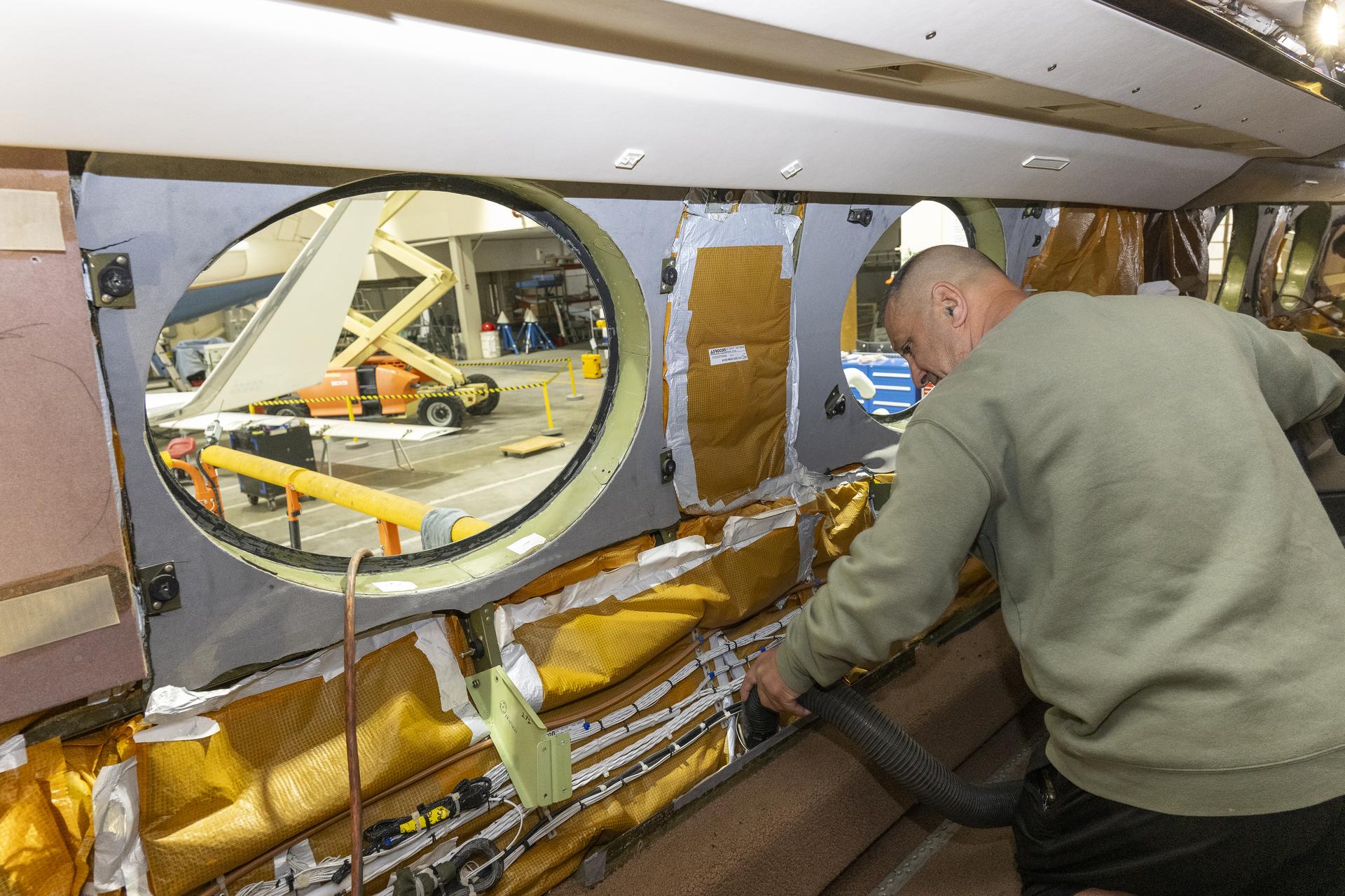 Eric Apikian, an aircraft mechanic, vacuums a NASA Gulfstream G-III aircraft compartment after wiring was added for sensors on Wednesday, Jan. 7, 2026, at NASA’s Armstrong Flight Research Center in Edwards, California. The modifications prepare the aircraft to join three others flying at different altitudes to capture a complete view of the Orion spacecraft’s heat shield during Artemis II reentry. This effort is part of NASA’s Scientifically Calibrated In-Flight Imagery project.