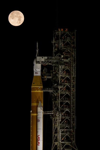 The Moon sets behind NASA’s Artemis II SLS (Space Launch System) rocket and O...
