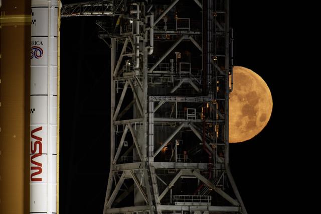 The Moon sets behind NASA’s Artemis II SLS (Space Launch System) rocket and O...