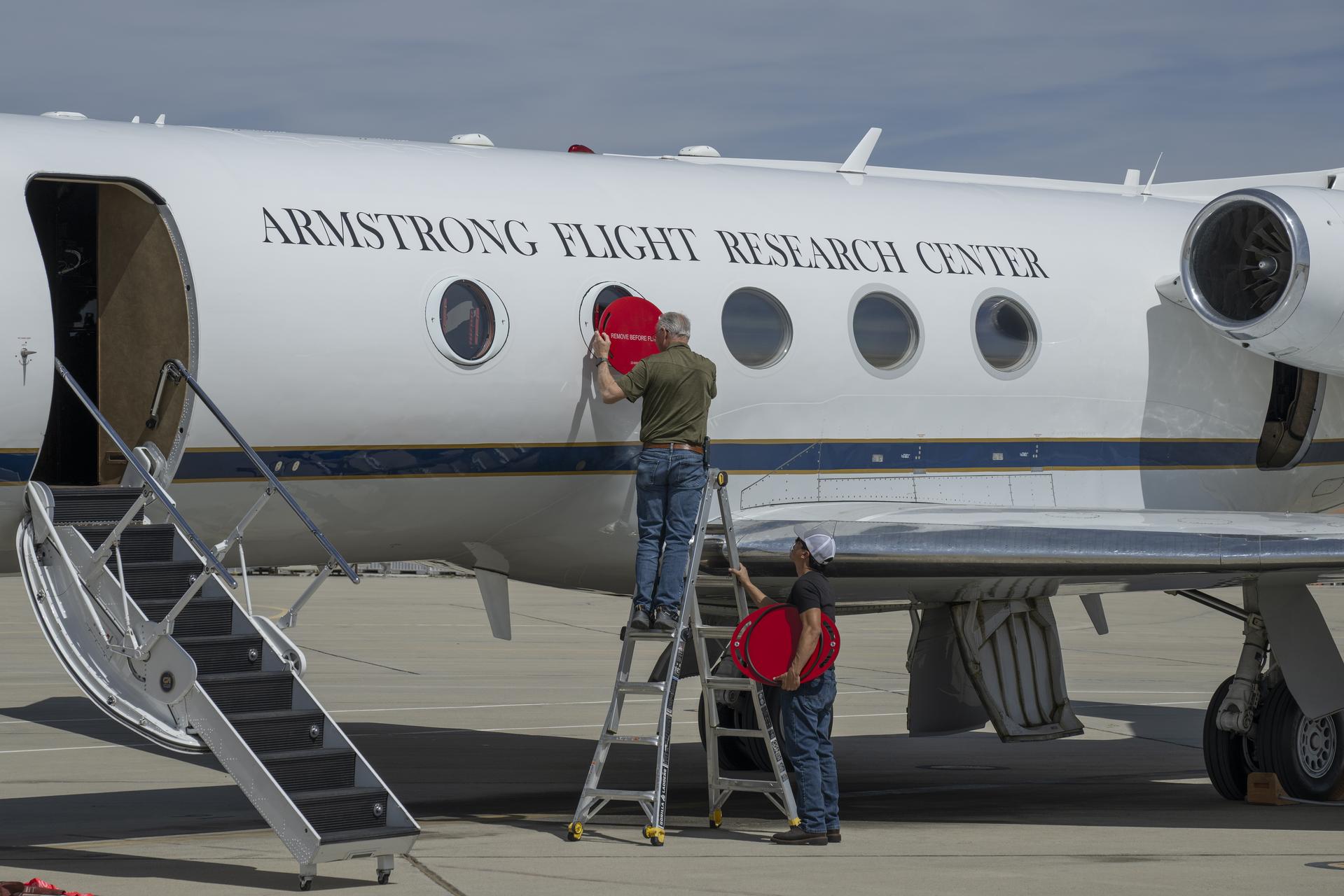 Scott Erickson, left, a quality assurance inspector, and Manny Rodriguez, Gulfstream G-III aircraft crew chief, remove window coverings from the aircraft on Friday, March 27, 2026, at NASA’s Armstrong Flight Research Center in Edwards, California. The G-III will join other NASA aircraft to capture imagery of the Orion spacecraft’s heat shield during Artemis II reentry. The mission is part of NASA’s Scientifically Calibrated In-Flight Imagery (SCIFLI) project, based at NASA’s Langley Research Center in Hampton, Virginia.