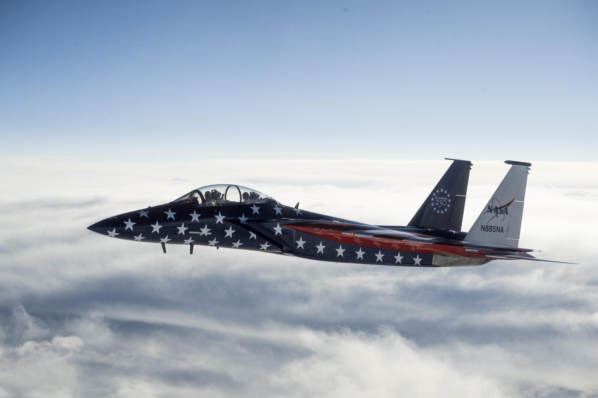 A red, white, and blue jet aircraft is shown during a cross‑country flight. The body of the aircraft is painted blue with white stars, and the wings are red and white stripes resembling the American flag.