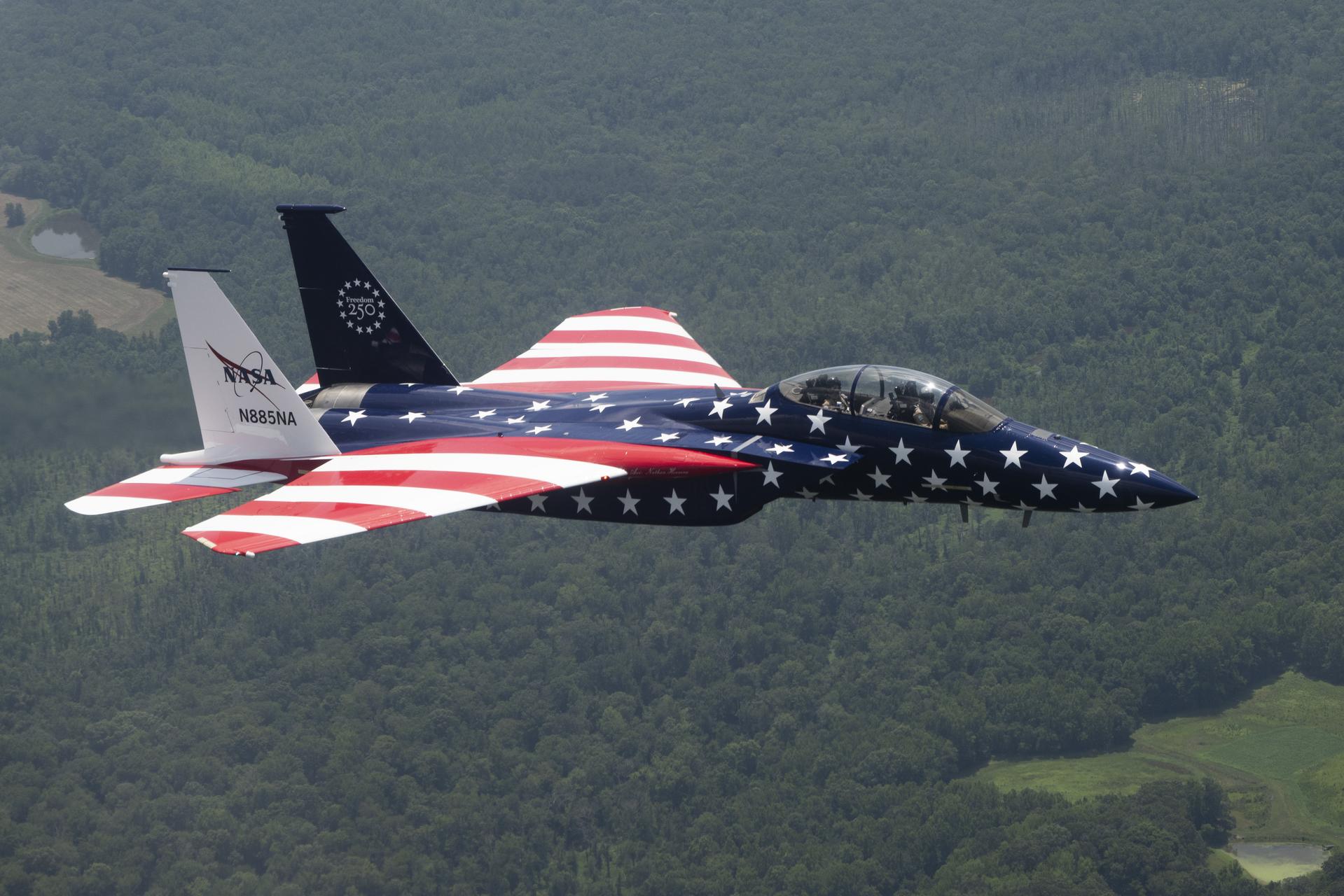 A jet aircraft painted in red, white and blue flies over green trees below.
