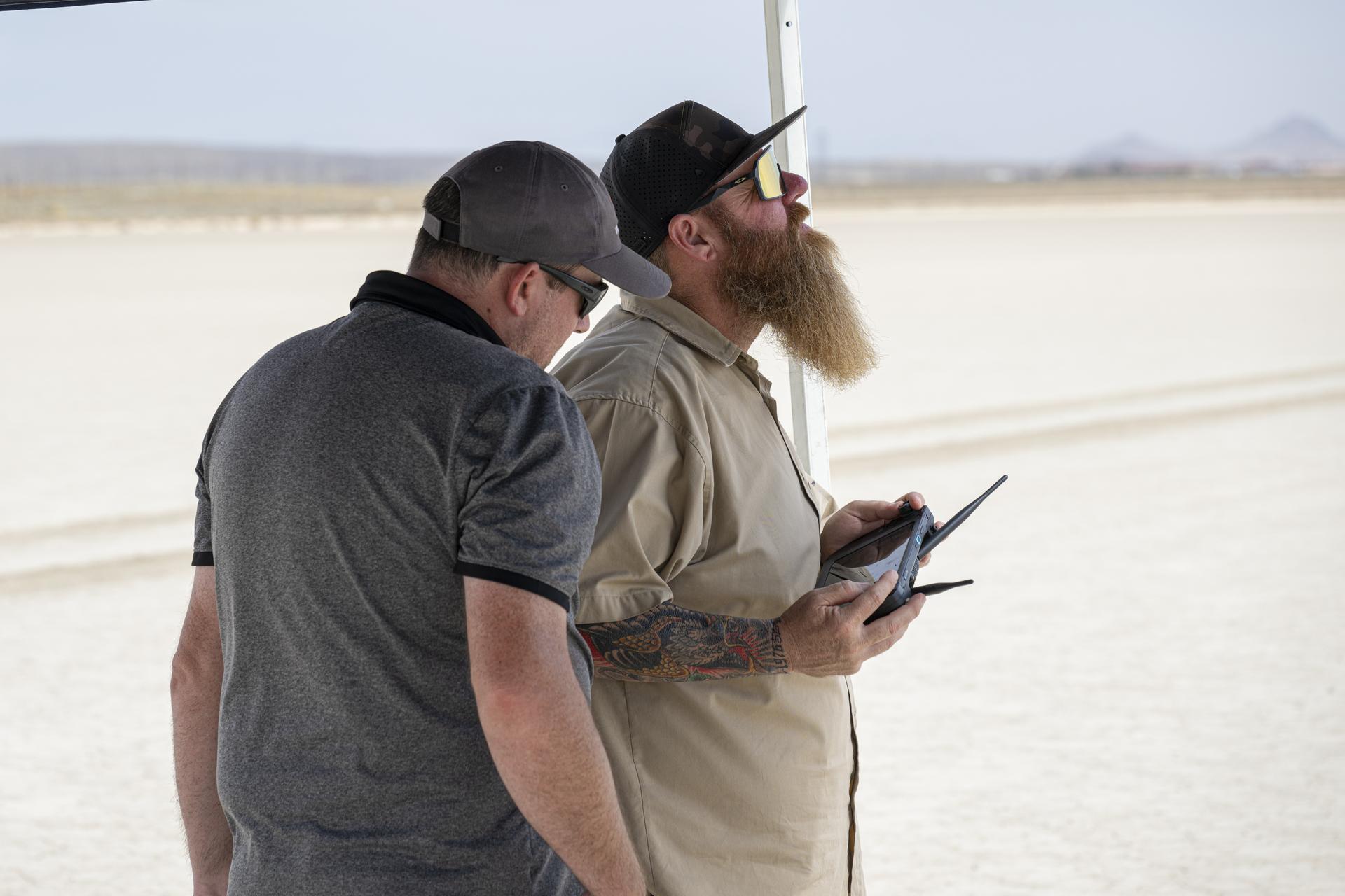 Justin Link, small uncrewed aircraft pilot, left, reads altitude data on a handheld display, as Justin Hall, Dale Reed Subscale Flight Research Laboratory chief pilot, flies NASA’s Alta-X drone near NASA’s Armstrong Flight Research Center in Edwards, California, on Thursday, Aug. 27, 2026. Researchers at NASA’s Johnson Space Center in Houston developed the advanced guidance and navigation system known as the Safe and Precise Landing – Integrated Capabilities Evolution (SPLICE) experiment, which is installed on the drone. SPLICE will help spacecraft land precisely and detect and avoid potential hazards, which is critical for NASA missions to the Moon and to Mars.