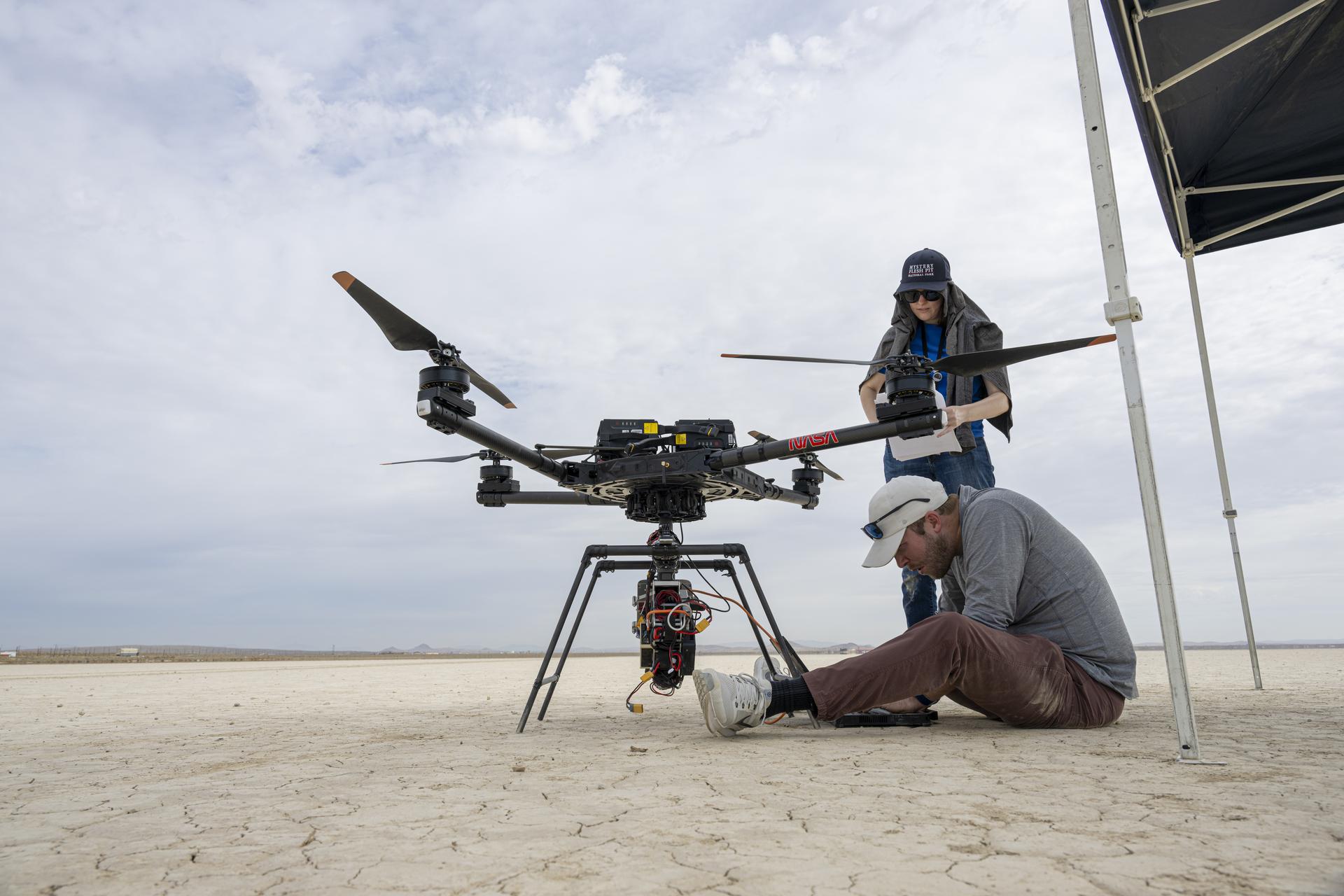 Davis Adams, project manager, sitting, and Jeanette Harper, flight software team member, check the guidance and navigation system known as the Safe and Precise Landing – Integrated Capabilities Evolution (SPLICE) experiment on an Alta-X drone near NASA’s Armstrong Flight Research Center in Edwards, California, on Thursday, Aug. 27, 2026. Researchers at NASA’s Johnson Space Center in Houston developed SPLICE, which recently completed simulated lunar descent and landing maneuvers. SPLICE will help spacecraft land precisely and detect and avoid potential hazards, which is critical for NASA missions to the Moon and to Mars.