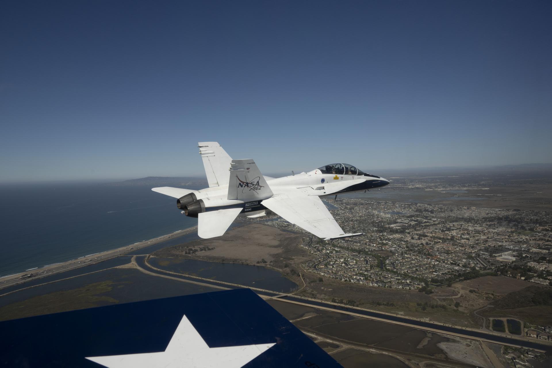 NASA test pilot Mike Lippert flies an F/A‑18 with videographer Lori Losey in the back seat during a Pacific Airshow flyover at Huntington Beach, California, Friday, Oct. 2, 2026. NASA is also hosting an exhibit featuring Artemis, the X‑59, SkyFall, a lunar globe, and an Apollo 15 Moon rock, with pilots and research experts available throughout the weekend.