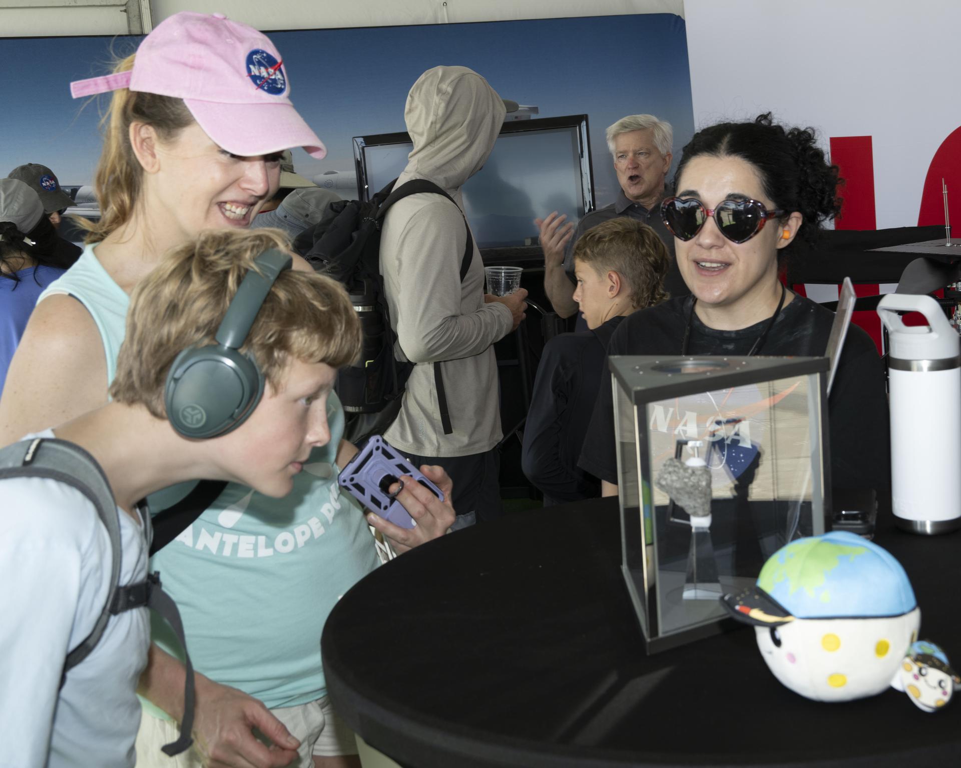 NASA public affairs specialist Arezu Sarvestani, right, speaks with visitors viewing the Apollo 15 Moon rock at NASA’s exhibit during the Pacific Airshow in Huntington Beach, California, Friday, Oct. 2, 2026. The exhibit also features Artemis, the X‑59, SkyFall, and a lunar globe. NASA aircraft will participate in the airshow from Oct. 2-4.