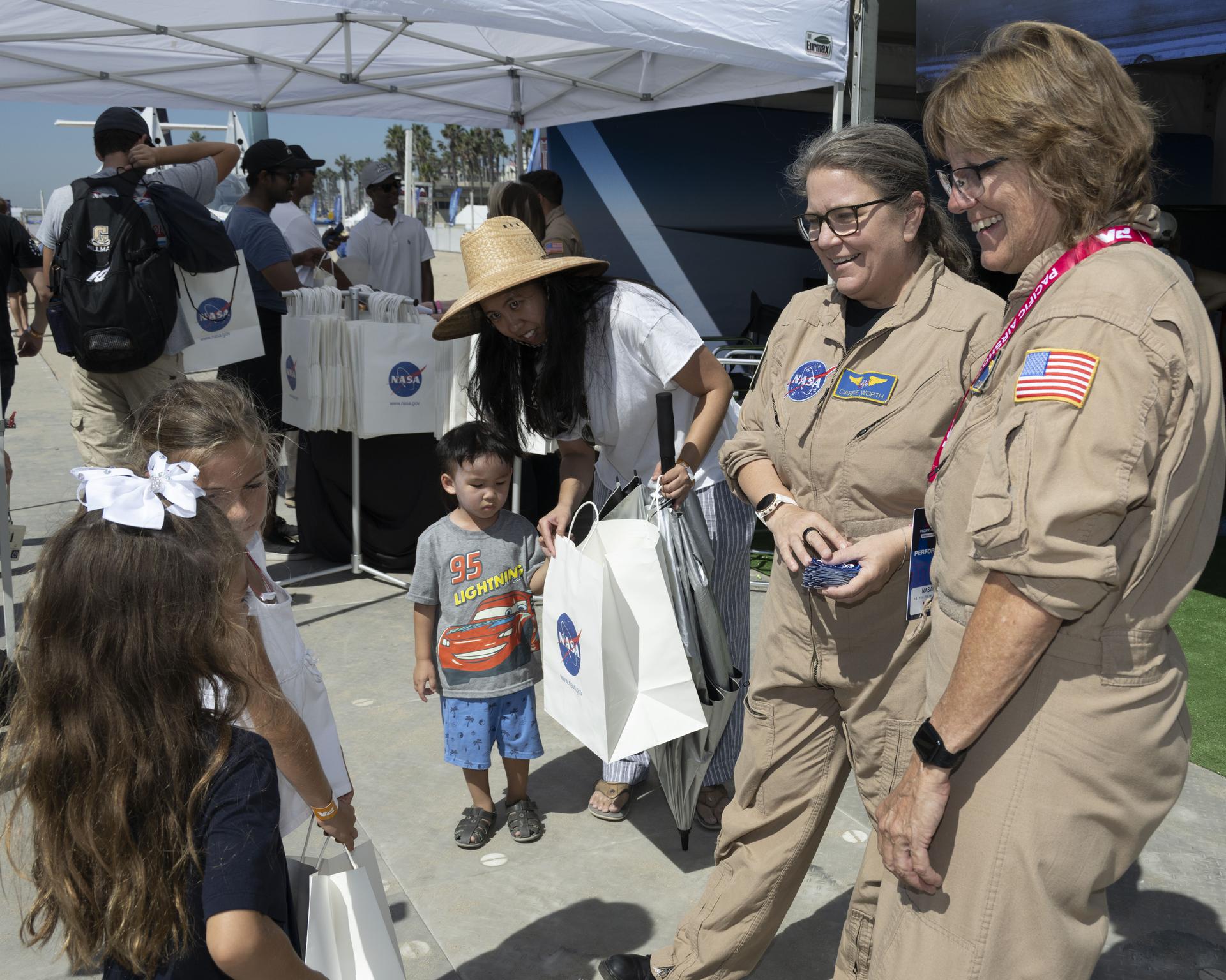 NASA videographer Lori Losey, right, and research pilot Carrie Worth speak with young visitors at the NASA exhibit during the Pacific Airshow at Huntington Beach, California, Friday, Oct. 2, 2026. The exhibit features Artemis, the X‑59, SkyFall, a lunar globe, and an Apollo 15 Moon rock.