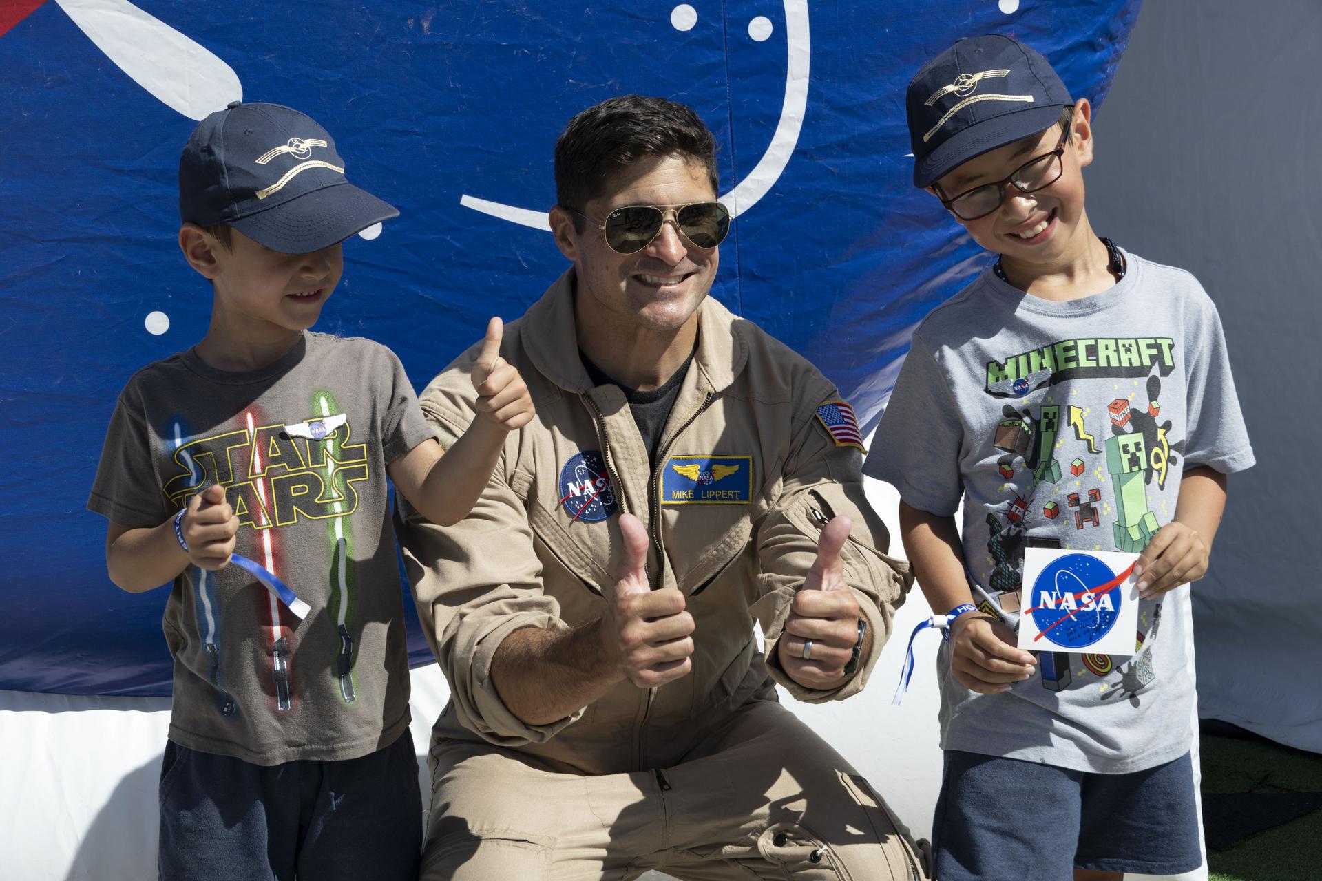 NASA test pilot Mike Lippert takes a photo with two young visitors at the NASA exhibit during the Pacific Airshow at Huntington Beach, California, Friday, Oct. 2, 2026. The exhibit features Artemis, the X‑59, SkyFall, a lunar globe, and an Apollo 15 Moon rock.