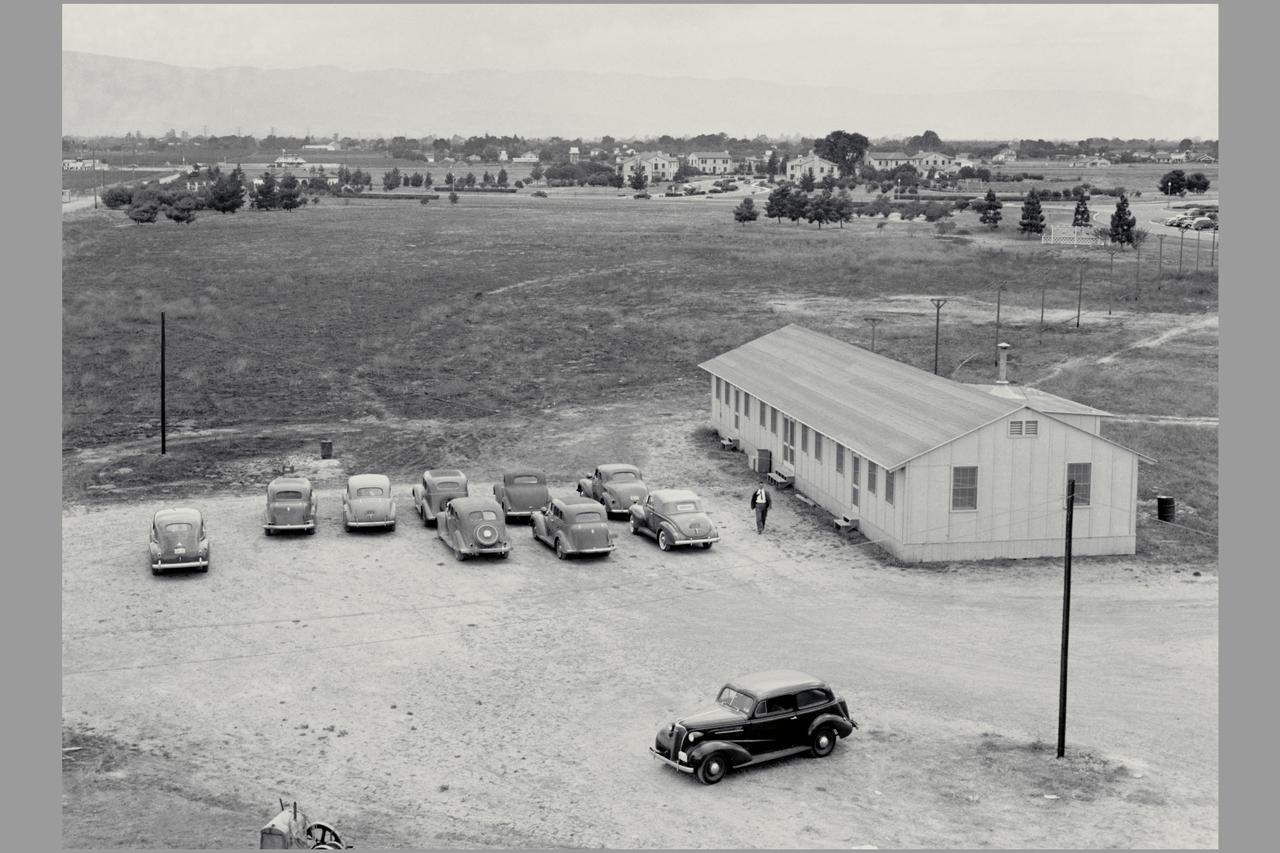 The original construction shack at Ames is featured in this view looking toward the southwest. Navy housing and buildings, still being utilized, can be observed in the center background.