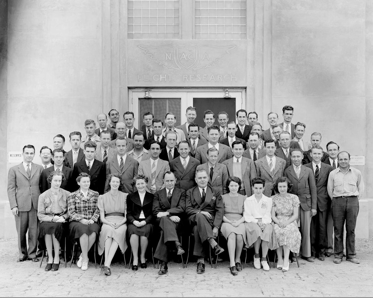 AMES STAFF STANDING IN FRONT OF THE NEW FLIGHT RESEARCH BUILDING. FROM LEFT TO RIGHT: FIRST ROW: M.U. NETTLE, M.A. WILLEY, M.H. DAVIES, M.W. ST. JOHN, S.J. DEFRANCE, E.R. SHARP, M.G. POOLE, V. BURGESS, R.A. PIPKIN. SECOND ROW: A.B. FREEMAN, T.W. O'BRIANT, L.T. VIDELL, C. F. WILSON,  R.M. FOSTER, M.C. MASSA, M.J. HOOD, C. BIOLETTI, C.W. FRICK, W.G. VINCENTI, H.W. KIRSCHBAUM, L. A. RODERT, E.C. BRAIG, C. GERBO. THIRD ROW: R.E. BROWNING, E.H. WOOD, R HUGHES, G BULIFANT, J.V. KELLEY, H.J. ALLEN, J. P. HOUSTON, K.S. BURCHARD, M. A. GREENE, FOURTH ROW: A. G. BUCK, E.W. BETTS, R.E. BRAIG, H.J. GOETT, J.F. PARSONS, H.S. DUNLAP, L.E. MINDEN, R.J. CLARKE.  FIFTH ROW: W.O. PETERSON, W. WALKER, C.H. HARVEY, J.C. DELANEY, T.W. MACOMBER, A.L. BLOCKER, N.K. DELANY, A.S. HERTZOG, R.R. NICKLE, P.T. PRIZLER, R.R. BENN, E.H.A. SCHNITKER.