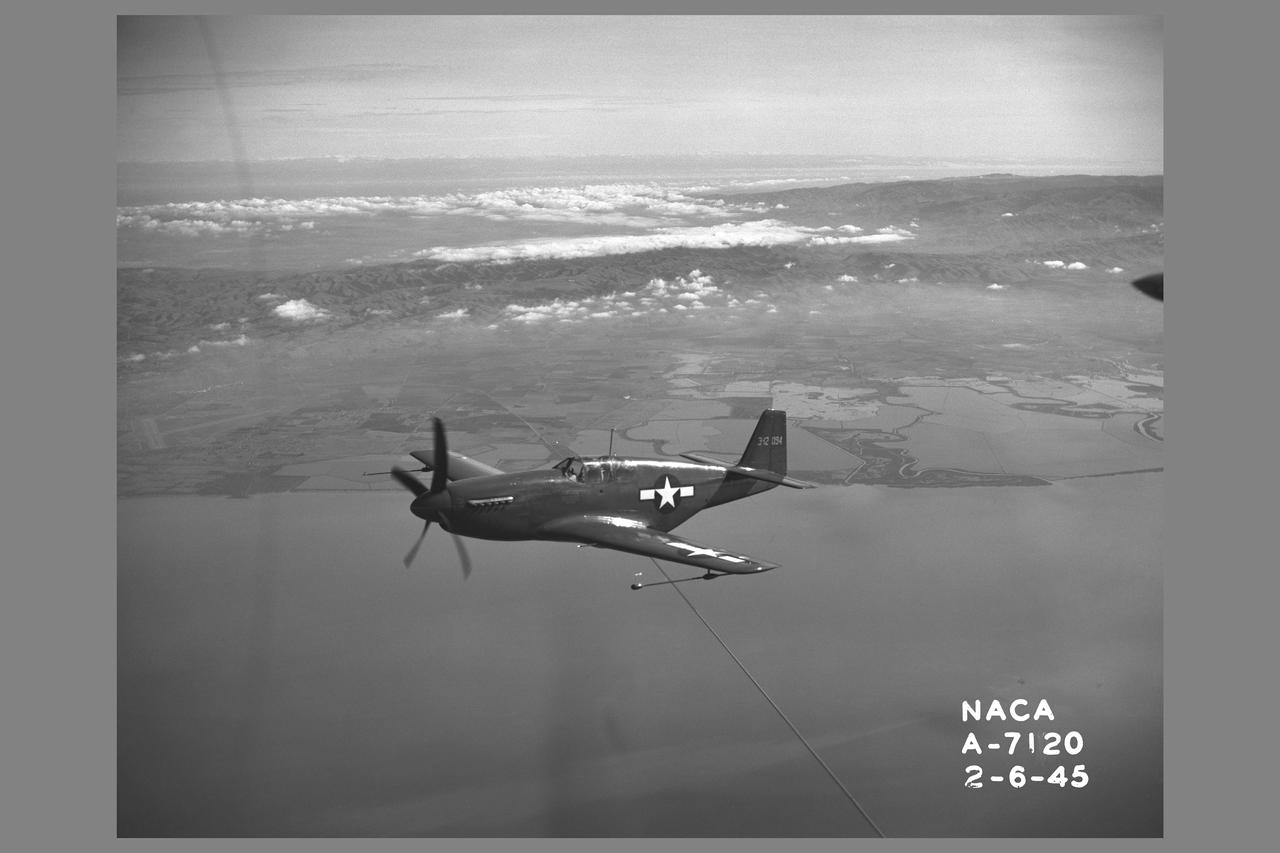 North American P-51B 'Mustang' fighter in flight over bay area. The P-51 with its new laminar-flow wing sections developed by NACA was the first airplane selected for testing of airplane drag in flight and wind tunnel comparison