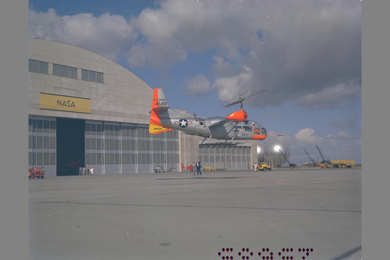 XV-3 HOVERING ON RAMP. Flight Test of Bell XV-3 Convertiplane. Bell VTOL tilt-rotor aircraft hovering in front of building N-211 at Moffett Field. The XV-3 design combined a helicopter rotor and a wing. A 450 horsepower Pratt & Whitney piston engine drove the two rotors. The XV-3, first flown in 1955 , was the first tilt-rotor to achieve 100% tilting of rotors. The vehicle was underpowered, however, and could not hover out of ground effect. Note the large ventral fin, which was added to imrpove directional stability in cruse (Oct 1962)