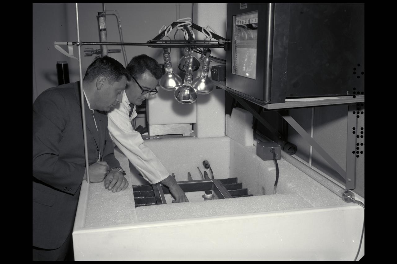 Dr H. 'Chuck' Klein (l) with Dr R. Young  looking into the Mars box (simulator), which simulated the environment of Mars for the preparation of life sciences experiments for the Viking lander.