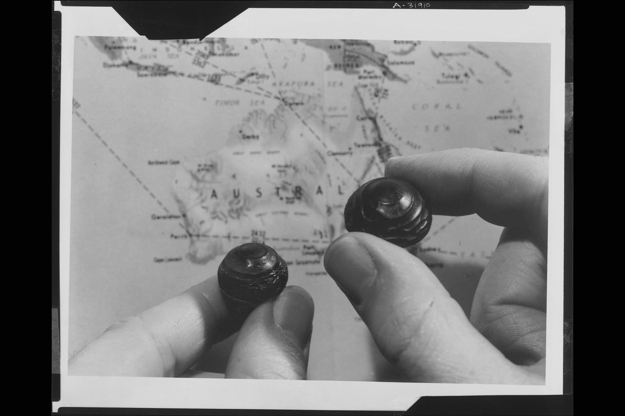 Dr. Dean R. Chapman a Ames Research Center scientists studing tektits, holding a simulated tektite created in the Ames arc jet facility (left) and authentic Australian tektite over a map of Australia.