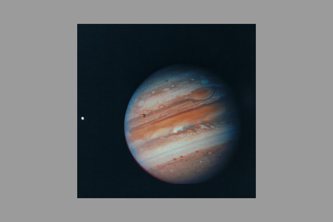 Photo by Voyager 1 (JPL) Jupiter, its Great Red Spot and three of its four largest satellites are visible in this photo taken Feb 5, 1979 by Voyager 1. The spacecraft was 28.4 million kilomters (17.5 million miles) from the planet at the time. The inner-most large satellite, Io, can be seen against Jupiter's disk. Io is distinguished by its bright, brown-yellow surface. To the right of Jupiter is the satellite Europa, also very bright but with fainter surface markings. The darkest satellite, Callisto (still nearly twice as bright as Earth's Moon), is barely visible at the bottom left of the picture. Callisto shows a bright patch in its northern hemisphere. All tThree orbit Jupiter in the equatorial plane, and appear in their present position because Voyageris above the plane. All three satellites show the same face to Jupiter always -- just as Earth's Moon always shows us the same face. In this photo we see the sides of the satellites that always face away from the planet. Jupiter's colorfully banded atmosphere displays complex patterns highlighted by the Great Red Spot, a large, circulating atmospheric disturbance. This photo was assembled from three black and white negatives by the Image Processing Lab at Jet Propulsion Laboratory. JPL manages and controls the Voyage Project for NASA's Office of Space Science. (ref: P-21083)