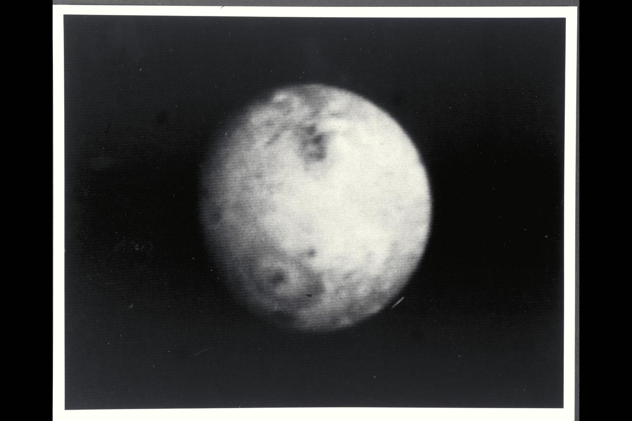 P-21739 BW Range: 4.7 million kilometers (2.9 million miles) This picture of Io was taken as Voyager 2 closes in on the Jovian system. Scientists are studying these distant views of Io for evidences of changes since Voyager 1 observations in March of  79. Voyager 1 discovered that Io, the innermost of the Galilean satellites, is the most volcanically active body yet seen in the solar system, surpassing even earth. In this picture, the first volcano discovered by Voyager 1 is again visible in the lower left portion of the disk as a dark oval with a dark spot in the center.  In March, this volcano appeared as a heart-shaped marking, not a symmetrical oval. Scientists believe that the non-symmetric markings earlier resulted from a constriction in the mouth of the volcanic vent causing erupting material to extrude preferentially in certain directions. Apparently, the volcanic eruptive activity, which sends material to altitudes of 280 kilometers (175 miles) or more above this volcano, has changed the vent geometry or dislodged an obstruction. Such changes in the form of eruptive fountains are common in terrestial volcanos, although on a much smaller scale than on Io.