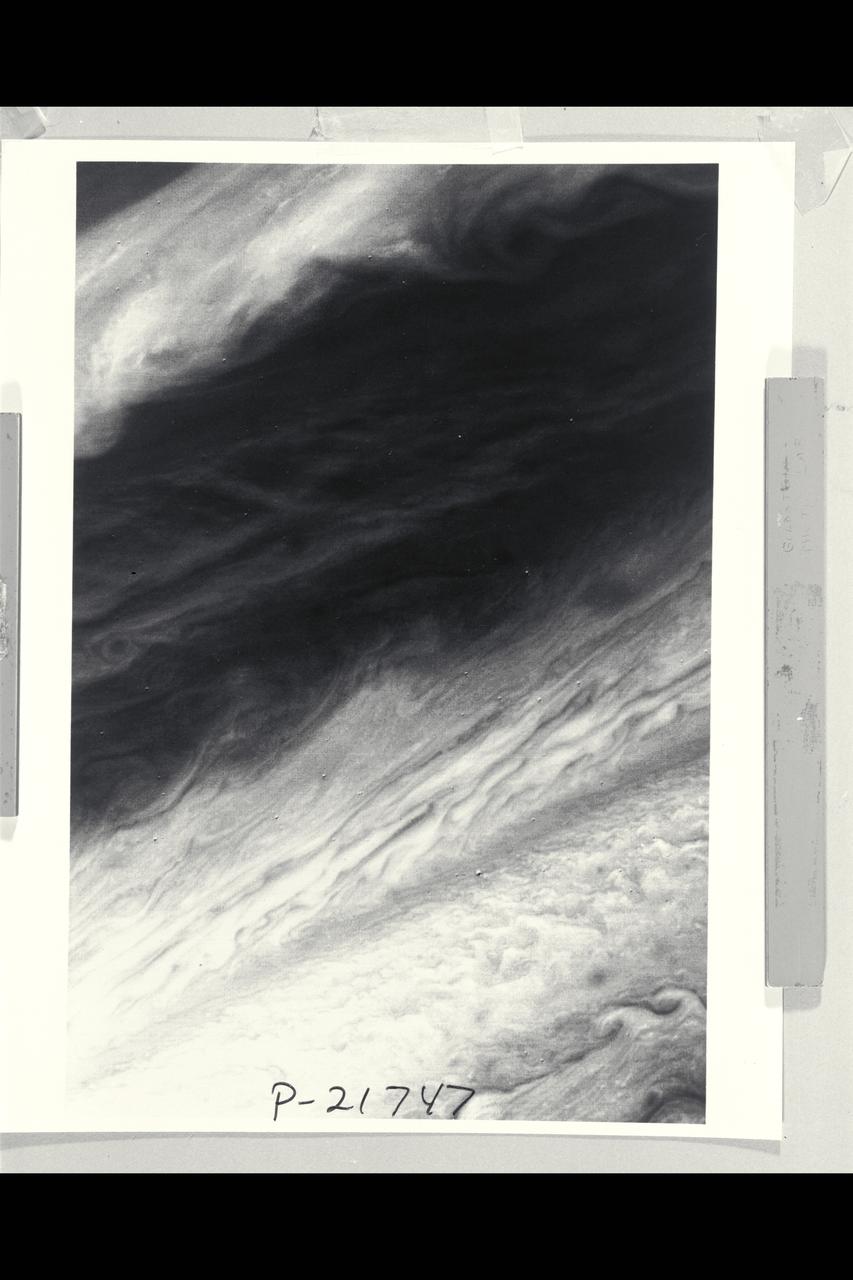 P-21747 BW Range: 2,200,000 miles This image shows a region of the Jovian atmosphere from approximately 25Â° N to the equatorial region. The north temperate jet, at approximately 23Â° N, where the wind speed is about 150 meters per second, is seen as a dark brown line from the left-hand edge to the right-hand corner of the picture. The wispy clouds of the north equatorial belt appear as shades of brown. The lower right-hand corner of the image shows the brighter (white) clouds of the equatorial region. A small blue area is apparent near the lower edge, which corresponds to a region free of the upper clouds, where it is possible to penetrate to cloud layers approximately 60 kilometers below the visible surface.