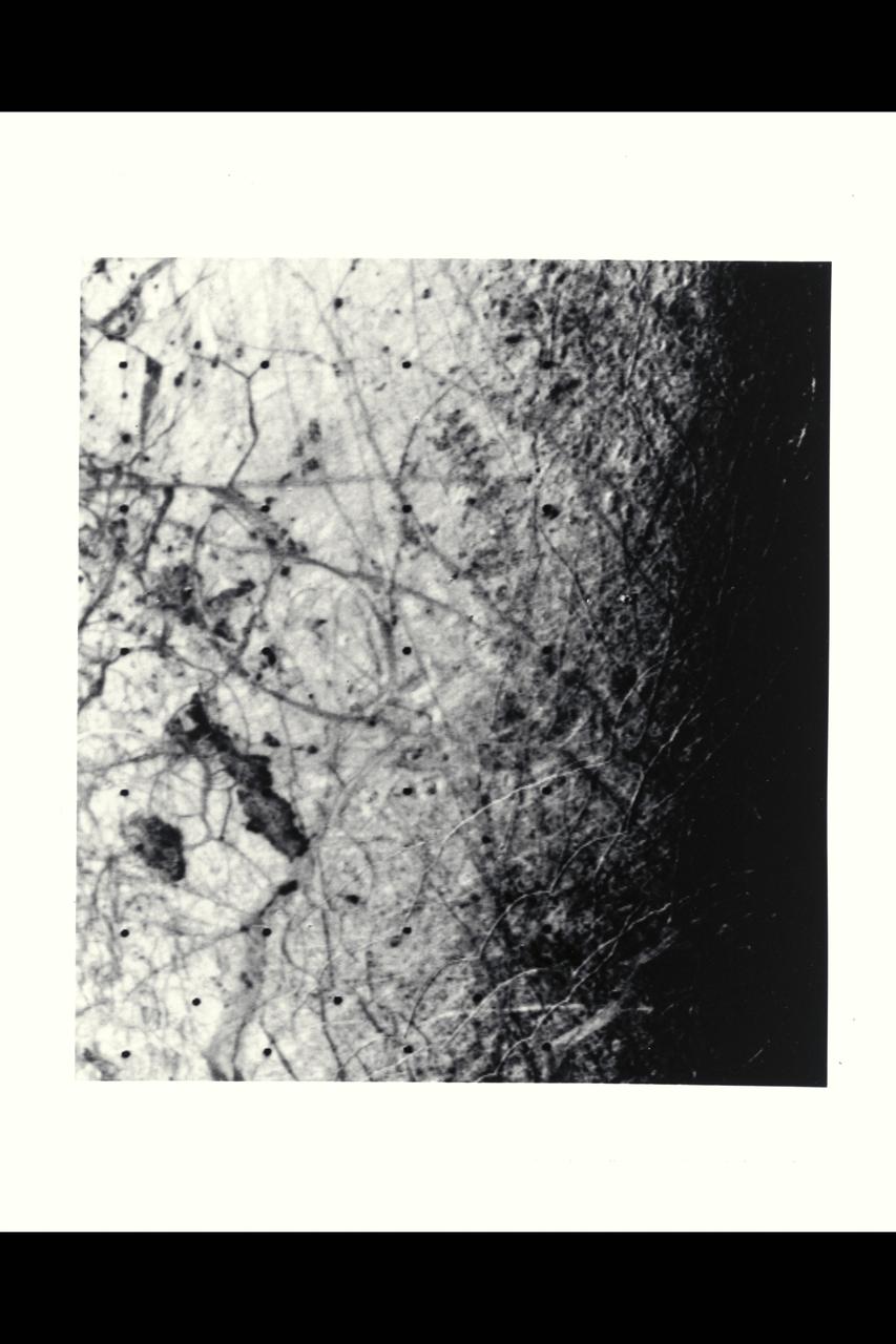 Range :  225,000 kilometers (140,625 miles) This image of the Jovian moon Europa was taken by Voyager 2 along the evening terminator, which best shows the surface topography of complex narrow ridges, seen as curved bright streaks, 5 to 10 kilometers wide, and typically 100 kilometers in length.  The area shown is about 600 by 800 kilometers, and the smallest features visible are about 4 kilometers in size.  Also visable are dark bands, more diffused in character, 20 to 40 kilometers wide and hundreds to thousands of kilometers in length.  A few features are suggestive of impact craters but are rare, indication that the surface thought to be dominantly ice is still active, perhaps warmed by tidal heating like Io.  The larger icy satellites, Callisto and Ganymede, are evidently colder with much more rigid crusts and ancient impact craters.  The complex intersection of dark markings and bright ridges suggest that the surface has been fractured and material from beneath has welled up to fill the cracks.