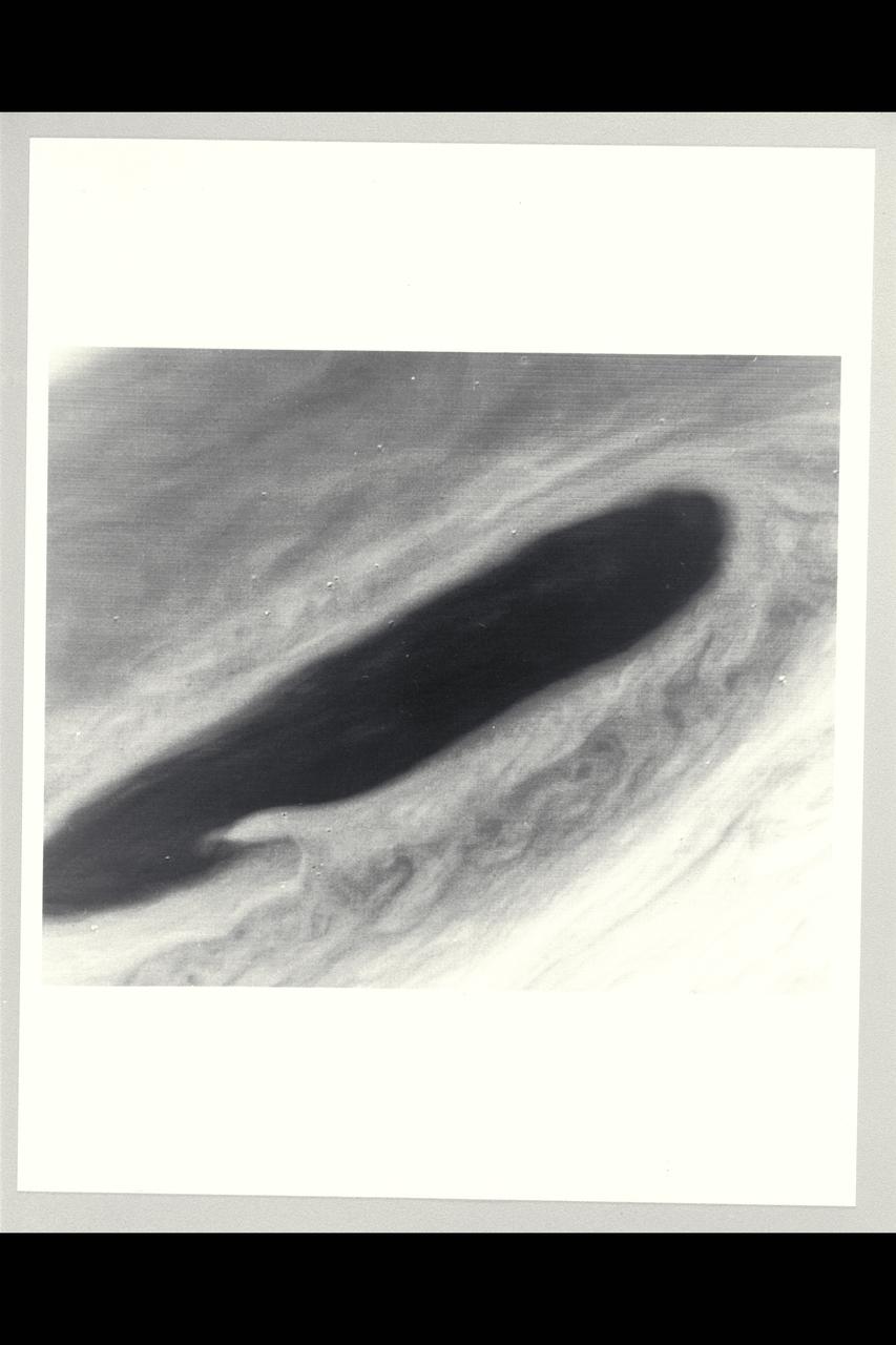 Range :  3.2 million km This image returned by Voyager 2 shows one of the long dark clouds observed in the North Equatorial Belt of Jupiter.  A high, white cloud is seen moving over the darker cloud, providing an indication of the structure of the cloud layers.  Thin white clouds are also seen within the dark cloud.