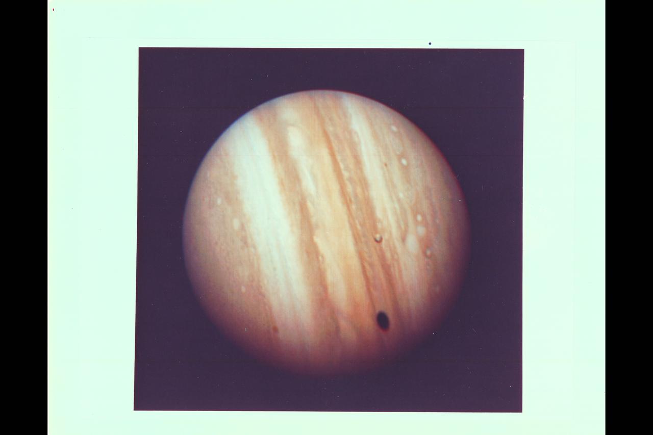 Photo by Voyager 1 Jupiter's satellite Io poses before the giant planet in this photo returned Jan 17, 1979 from a distance of 29 million miles (47 million kilometers). The satellite's shadow can be seen falling on the face of Jupiter at left. Io is traveling from left to right in its one-and-three-quarter-day orbit around Jupiter. Even from this great distance the image of Io shows dark poles and bright equatorial region. Voyager 1 will make its closest approach to Jupiter  174, 000 miles (280,000 kilometer) on March 5. It will then continue to Saturn in November 1980. This color photo was assembled at Jet Propulsion Laboratory's Image Processing Lab from three black and white images taken through filters. The Voyagers are managed for NASA's Office of Space Science by Jet Propulsion Laboratory. (JPL Ref: P-20946C)