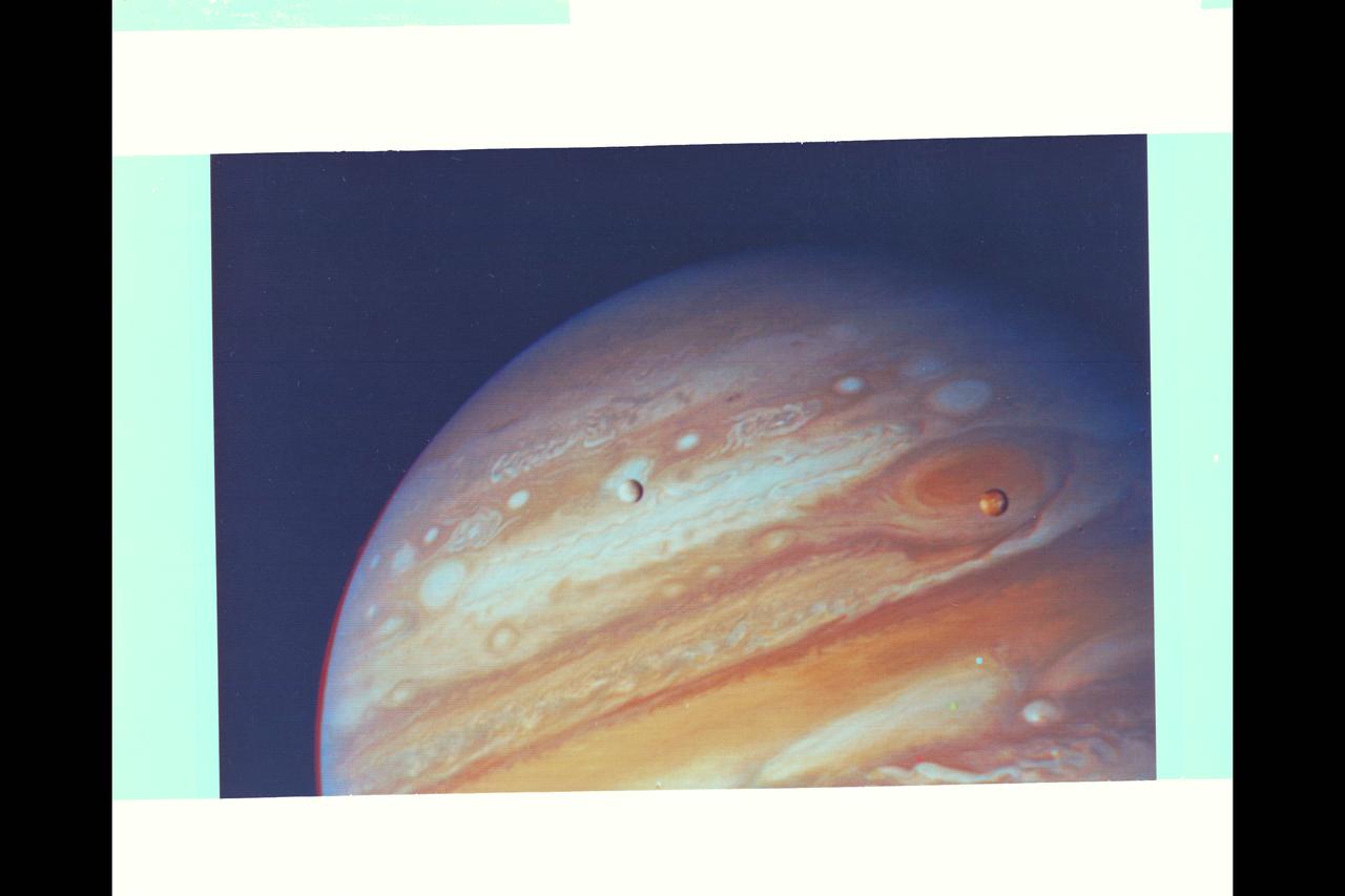 Voyager 1 Image of Jupiter and two of its satellites (Io, left, and Europa). Io is about 350,000 kilometers (220,000 miles) above Jupiter's Great Red Spot; Europa is about 600,000 kilometers (375,000 miles) above Jupiter's clouds. Although both satellites have about the same brightness, Io's color is very different from Europa's. Io's equatorial region show two types of material -- dark orange, broken by several bright spots -- producing a mottled appearance. The poles are darker and reddish. Preliminary evidence suggests color variations within and between the polar regions.  Io's surface composition is unknown, but scientists believe it may be a mixture of salts and sulfur.  Erupoa is less strongly colored, although still relatively dark at short wavelengths. Markings on Eruopa are less evident that on the other satellites, although this picture shows darker regions toward the trailing half of the visible disk. Jupiter at this point is about 20 million kilometers (12.4 million miles) from the spacecraft.  At this resolution (about 400 kimometers or 250 miles) there is evidence of circular motion in Jupiter's atmosphere. While the dominant large-scale motions are west-to-east, small-scale movement includes eddy-like circulation within and between the bands.  (JPL ref: P-21082)